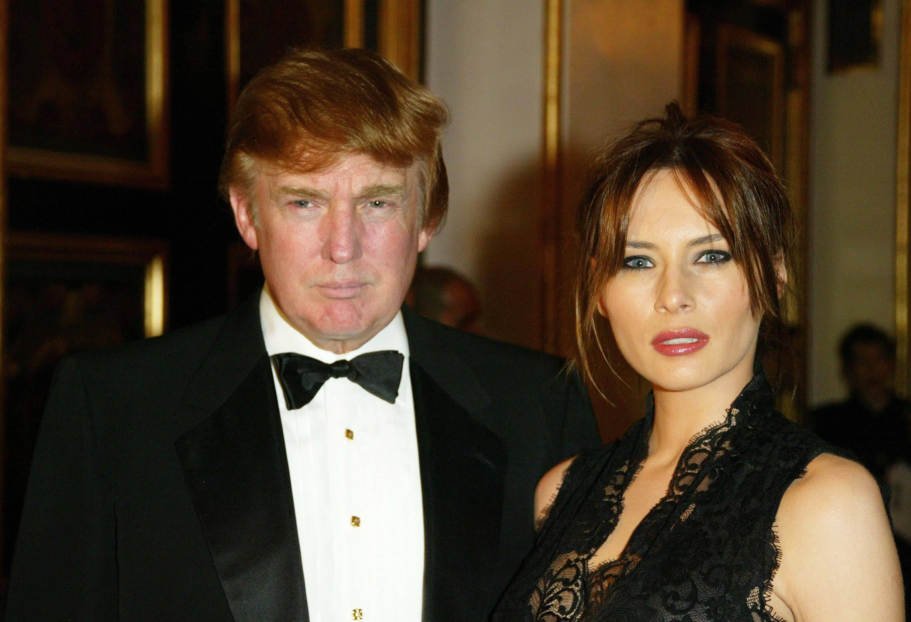 Melania 桌布 壁紙 — 一位身穿黑色燕尾服的男士和一位身穿黑色蕾絲裙的女士在優雅的室內活動中合影。