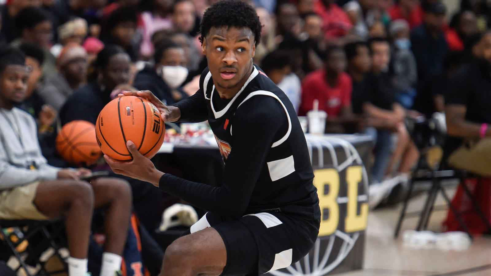 Bronny James 桌布 壁紙 — 一位身穿黑色球衣、專注的籃球運動員在觀眾背景下的激烈比賽中運著橙色球。