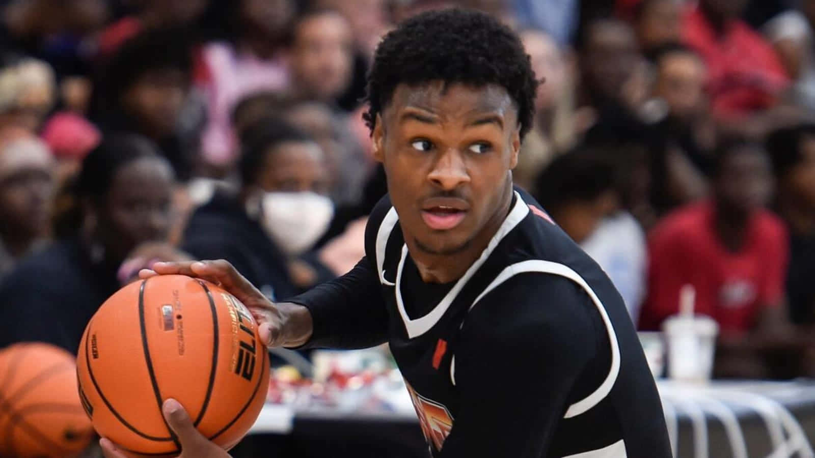 Bronny James 桌布 壁紙 — 一位身穿黑色球衣、專注的籃球運動員在比賽中帶著強烈的專注力運球橙色球。