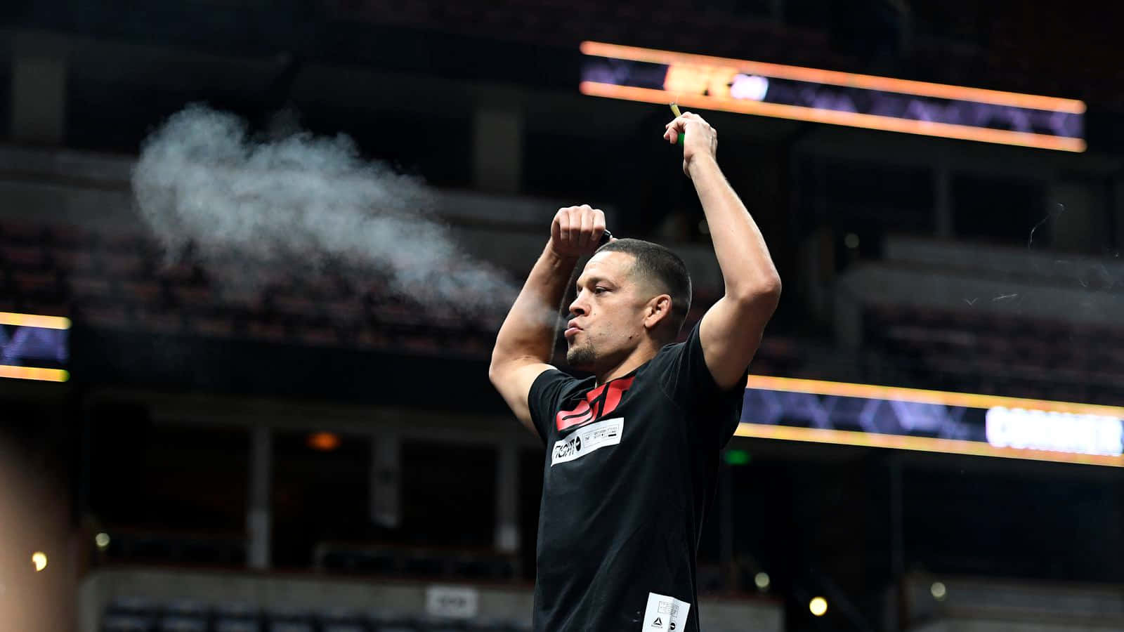 UFC 桌布 壁紙 — 一位身穿黑色球衣的專注運動員在昏暗的場館中舉起雙臂慶祝，手中冒出煙霧。