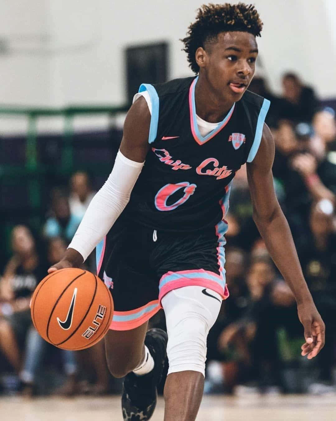 Bronny James 桌布 壁紙 — 一位身穿黑色球衣的年輕籃球運動員在室內比賽中專注地運著橙色籃球。