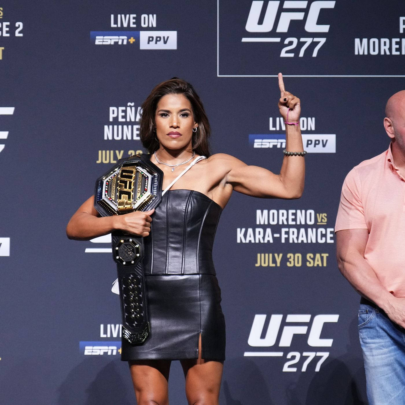 UFC 桌布 壁紙 — 一位身穿黑色皮裙的女性UFC拳手在記者會上高舉冠軍腰帶並向上指。