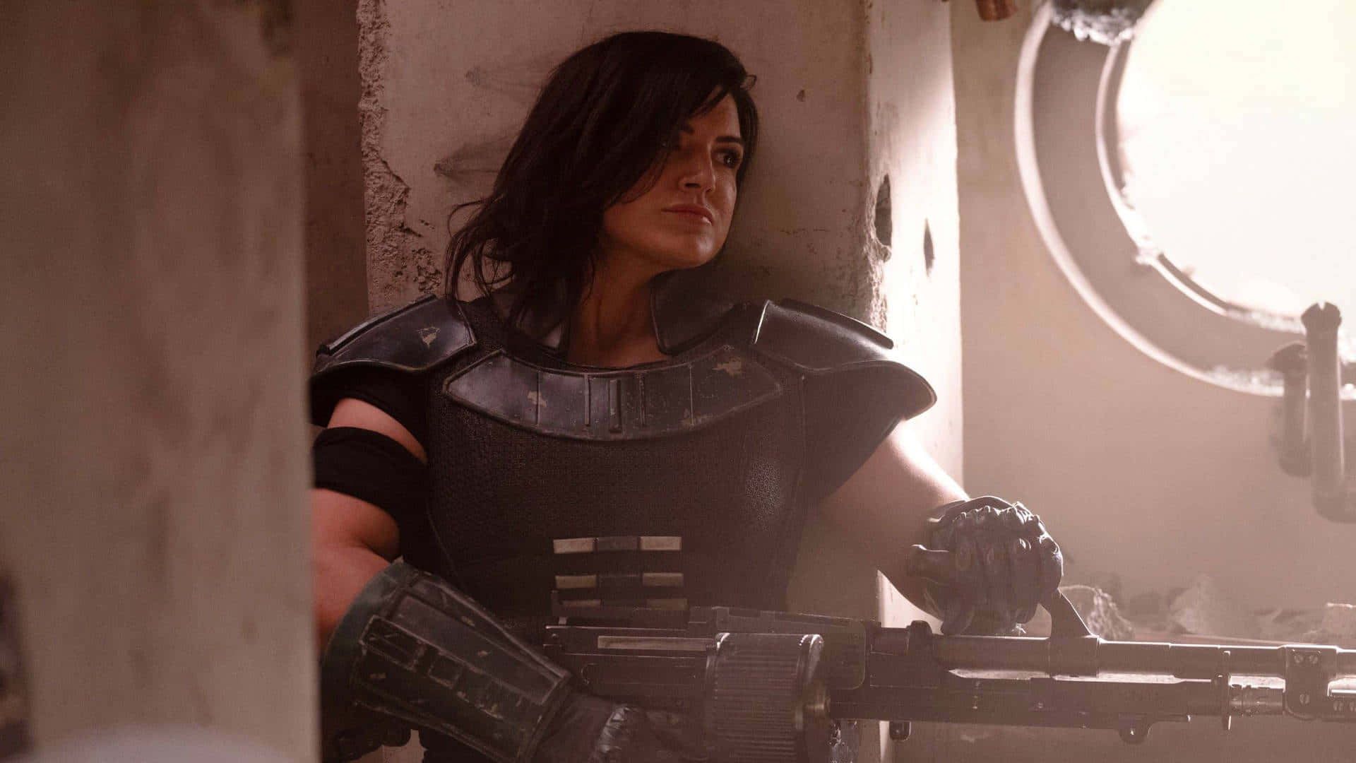 Mandalorian Pc 桌布 壁紙 — 一位身穿黑色盔甲的女兵在塵土飛揚、陽光照耀的廢墟走廊中手持重型武器。