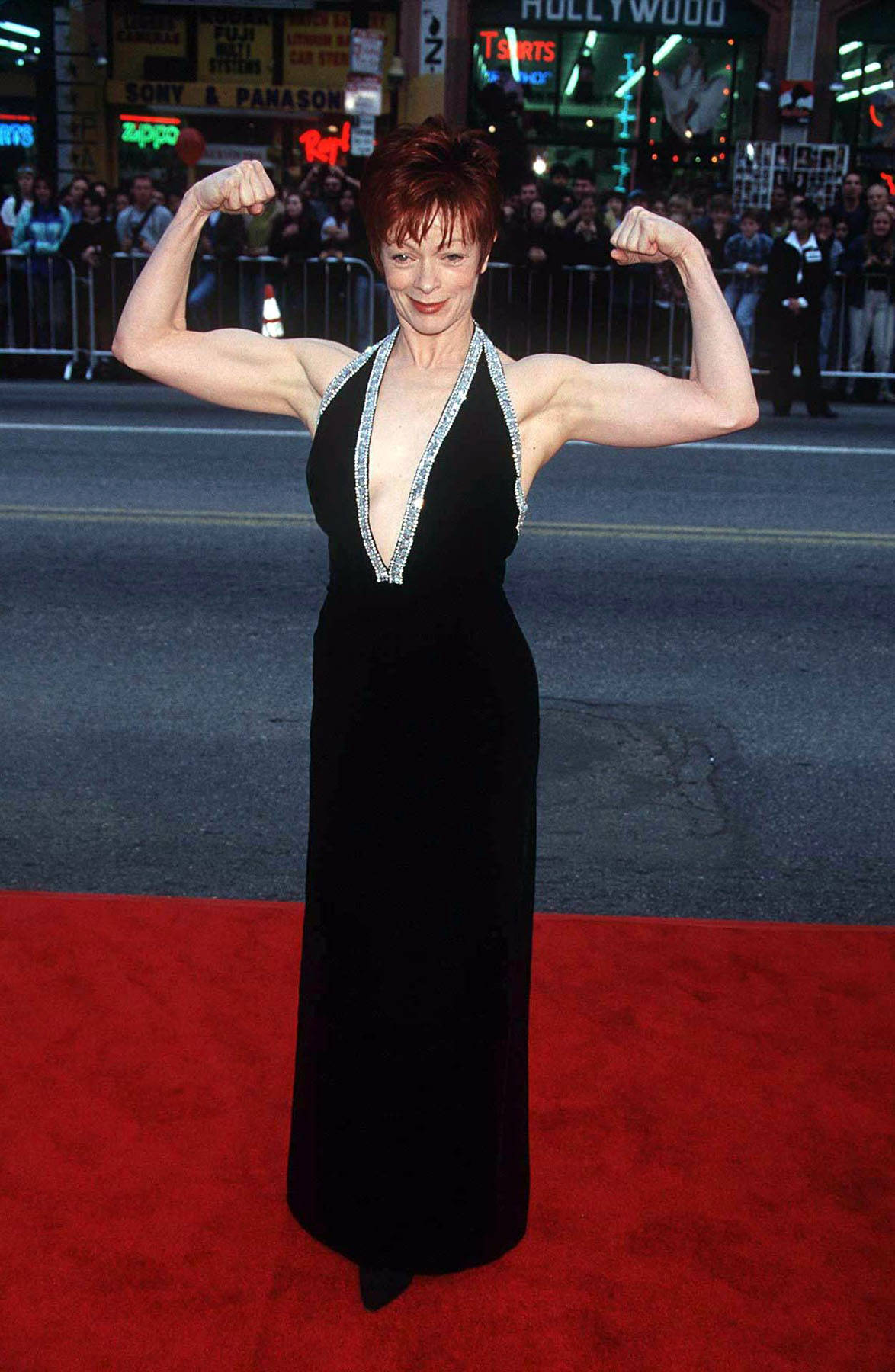 Celebrity 桌布 壁紙 — 一位身穿黑色禮服的女士在好萊塢標誌和人群前的紅地毯上展示肌肉。
