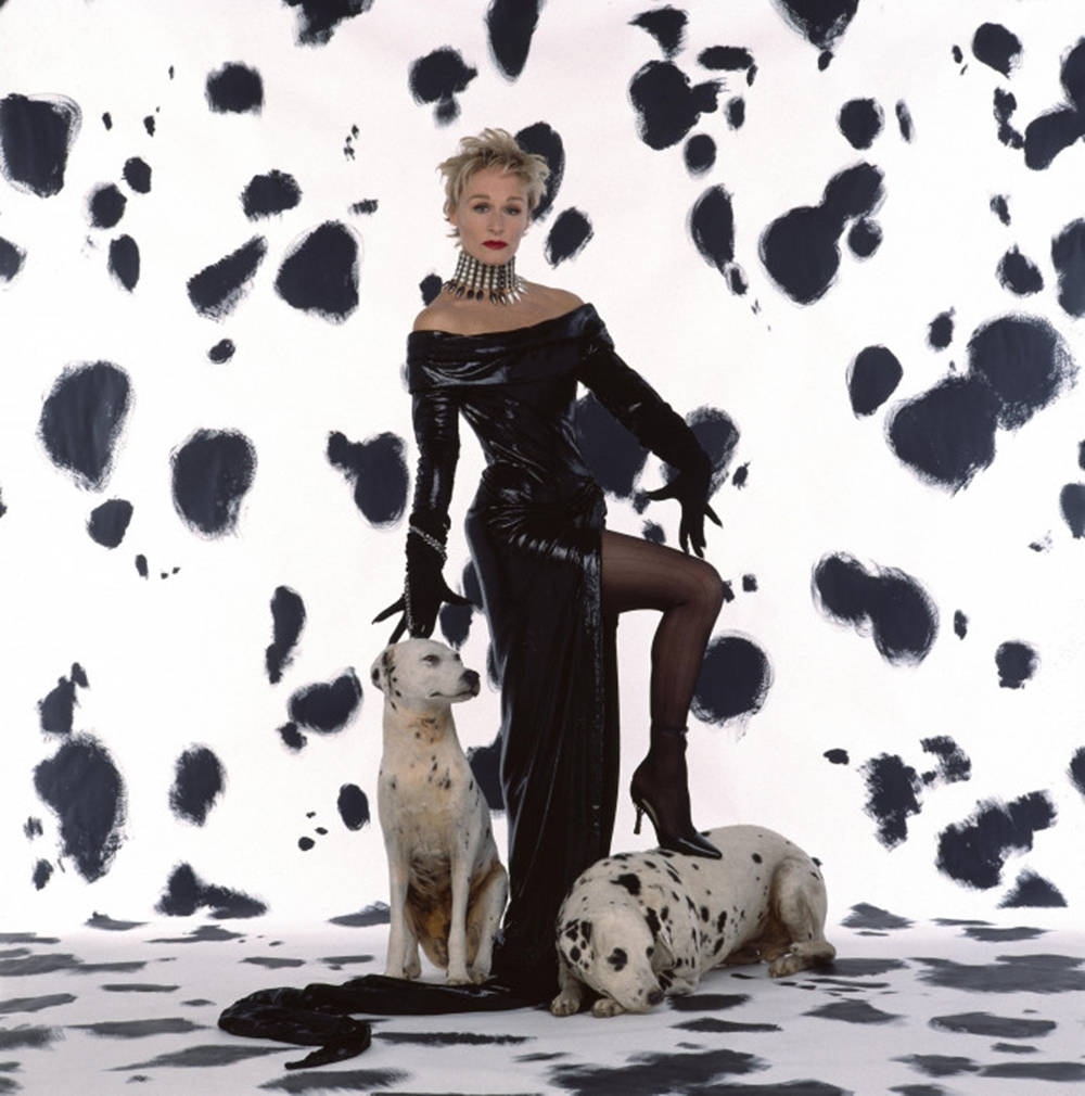 101 Dalmatians 桌布 壁紙 — 一位身穿黑色禮服的女士與兩隻斑點狗在醒目的黑白斑點背景前擺姿勢。