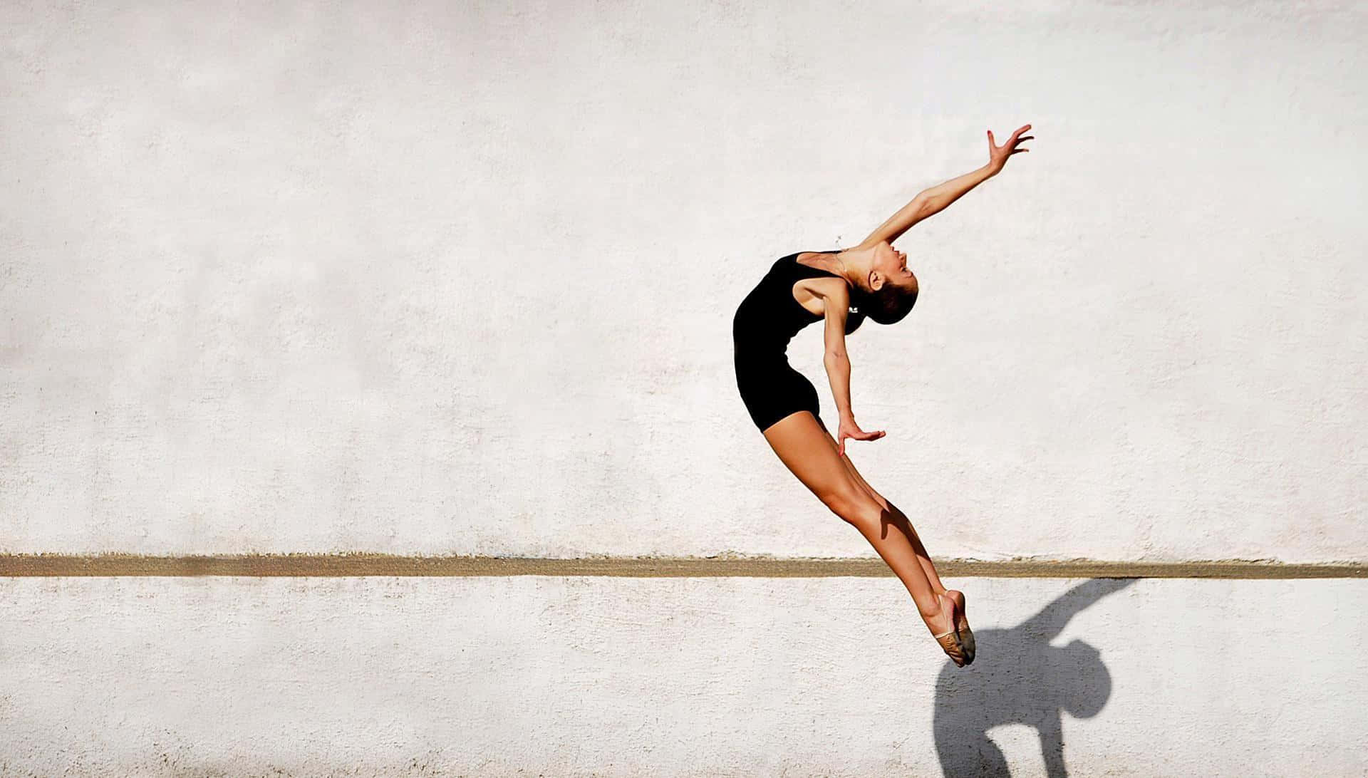 Ballet 桌布 壁紙 — 一位身穿黑色緊身衣的舞者，在純白牆壁前優雅躍起，投下清晰的影子。