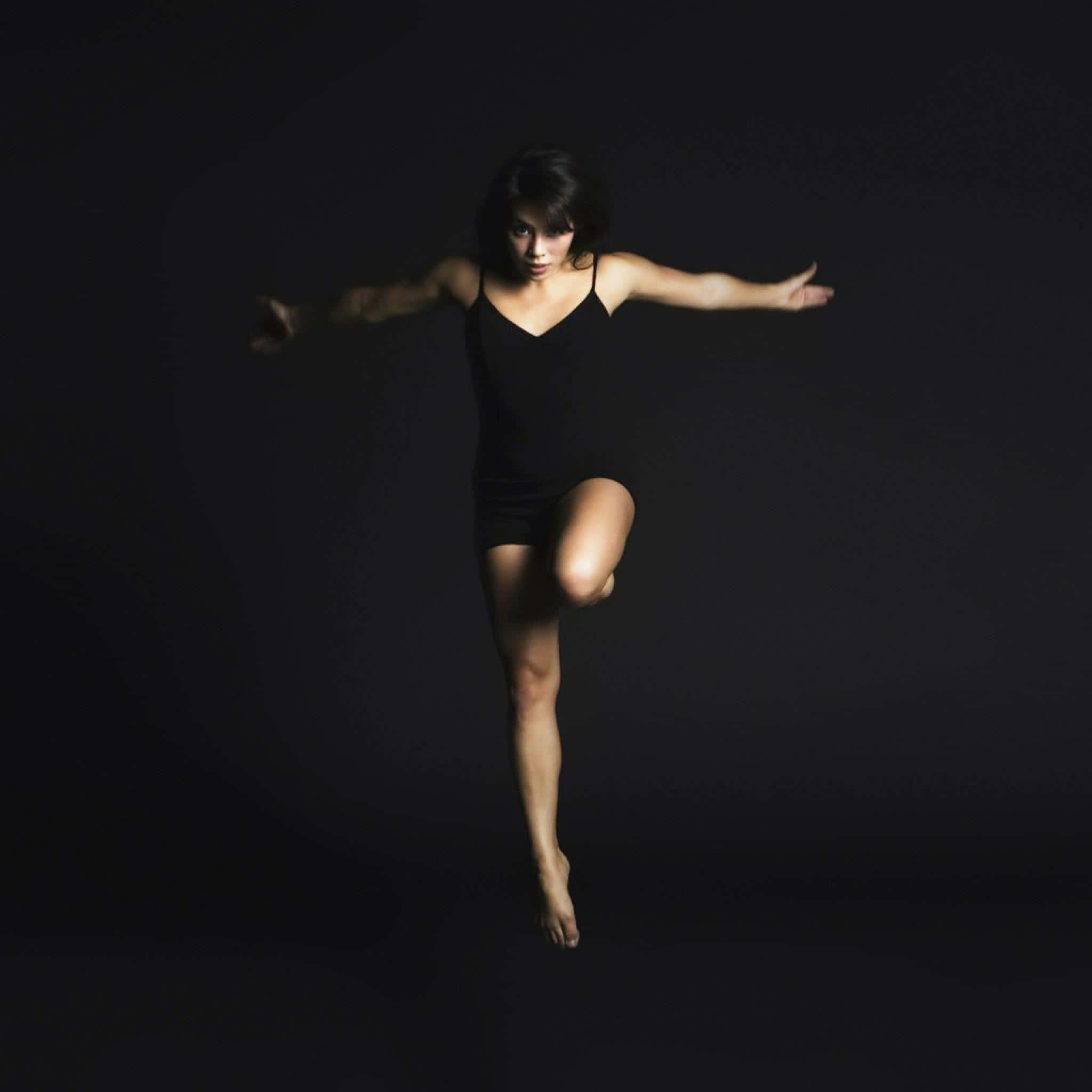 Ballet Dancer 桌布 壁紙 — 一位身穿黑色緊身衣的舞者在黑暗的攝影棚背景下，於戲劇性的聚光燈中騰空跳躍。