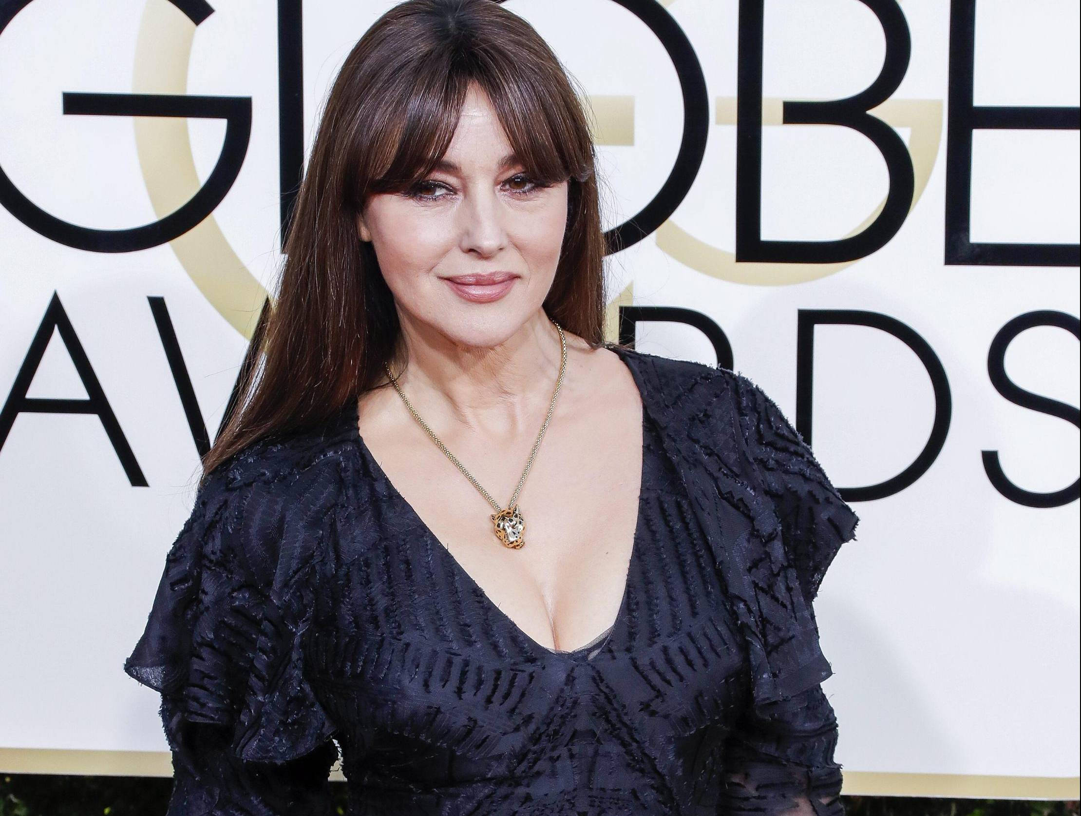 monica bellucci 桌布 壁紙 — 一位身穿黑色荷葉邊連衣裙的女性在金球獎背景前對著鏡頭微笑。