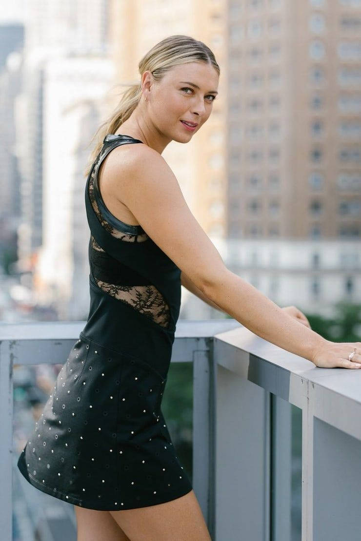 Celebrity 桌布 壁紙 — 一位身穿黑色蕾絲和亮片連衣裙的女性，隨意地靠在城市陽台欄杆上，身後是模糊的摩天大樓。