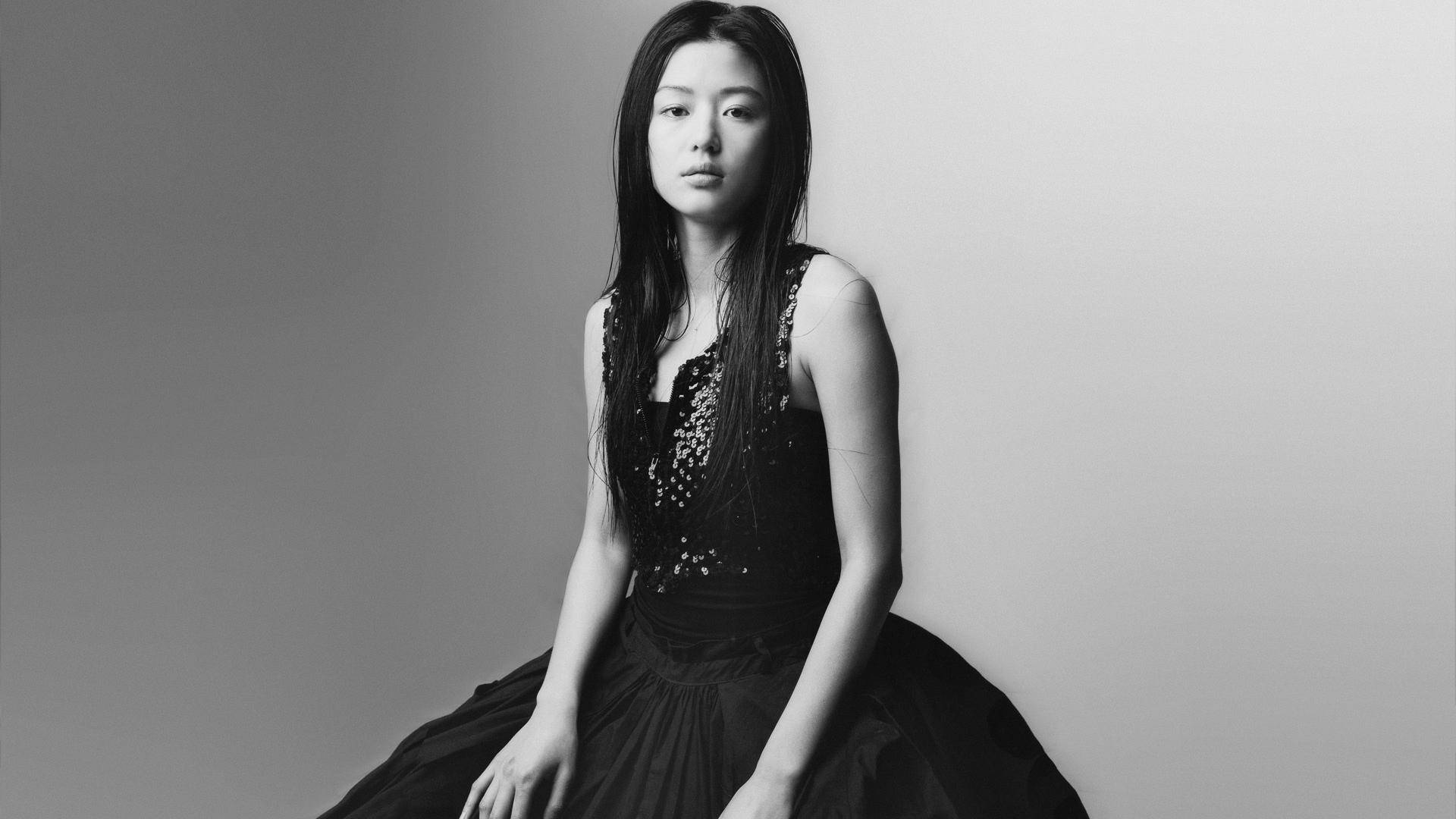 Jun Ji Hyun 桌布 壁紙 — 一位身穿黑色蕾絲裙的優雅女士坐在純灰色背景前，呈現出鮮明的黑白肖像。
