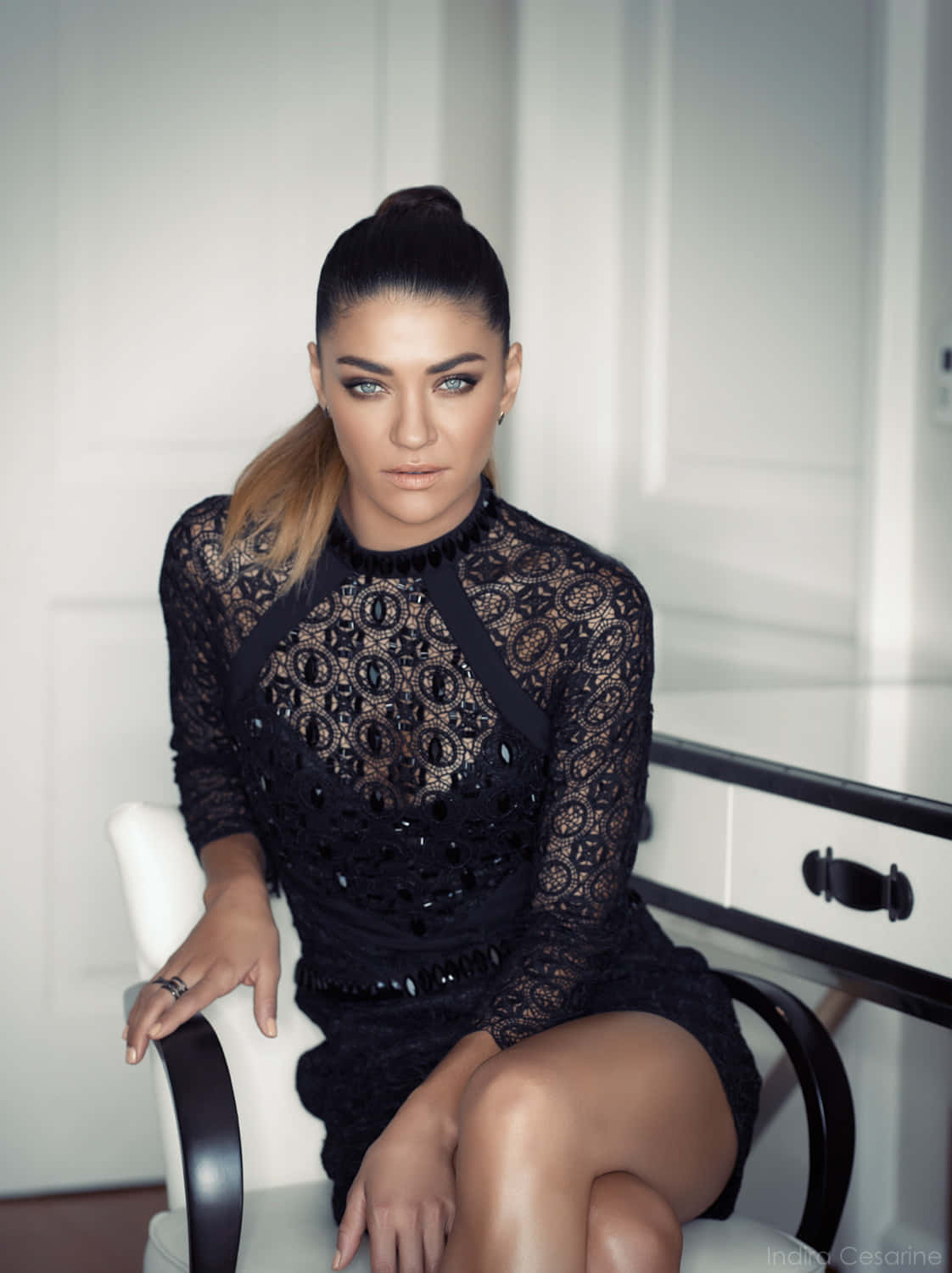 jessica szohr 桌布 壁紙 — 一位身穿黑色蕾絲連衣裙的優雅女性，自信地坐在白色椅子上，背景是簡約的白色室內設計。