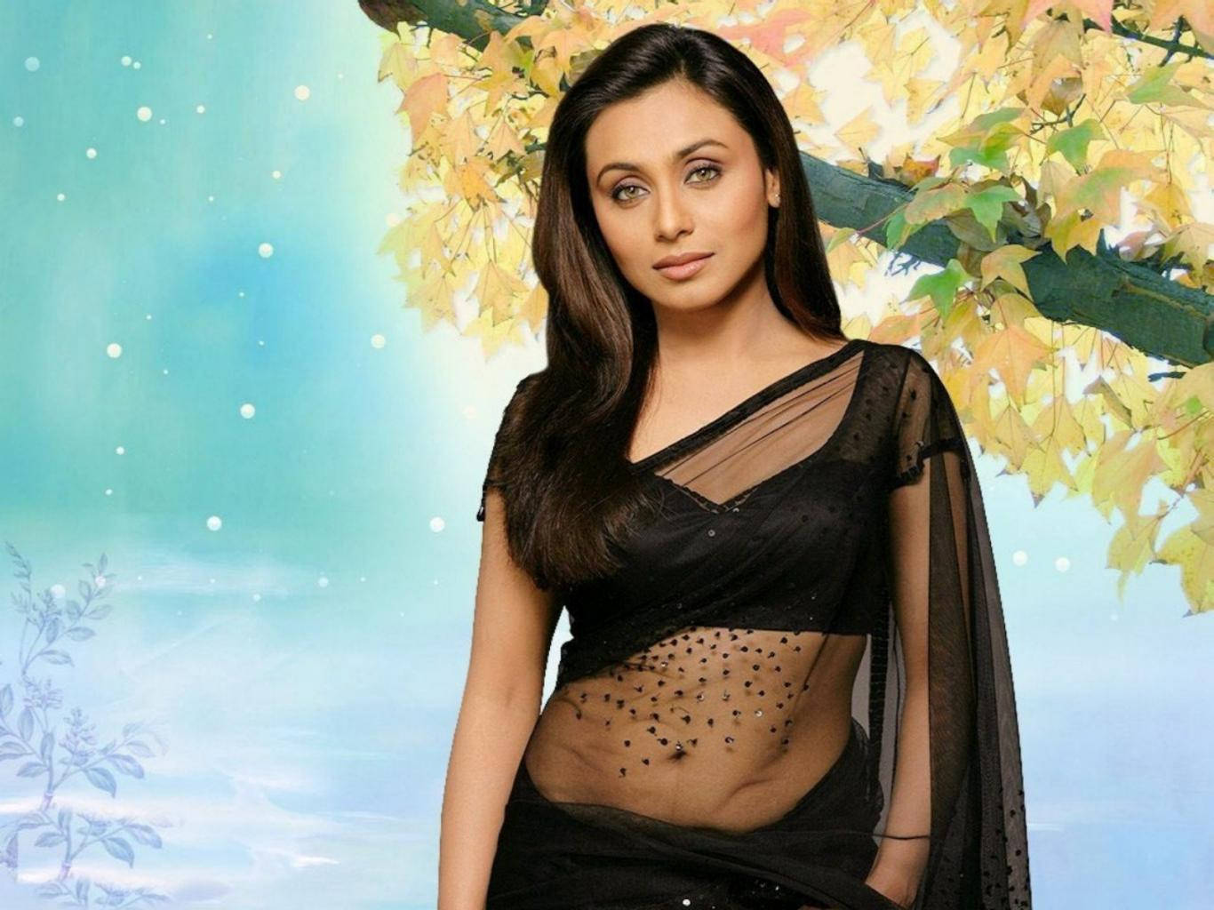 Rani Mukerji 桌布 壁紙 — 一位身穿黑色薄紗紗麗的女性站在金色秋葉下，背景是柔和的藍天，飄浮著白色點點。