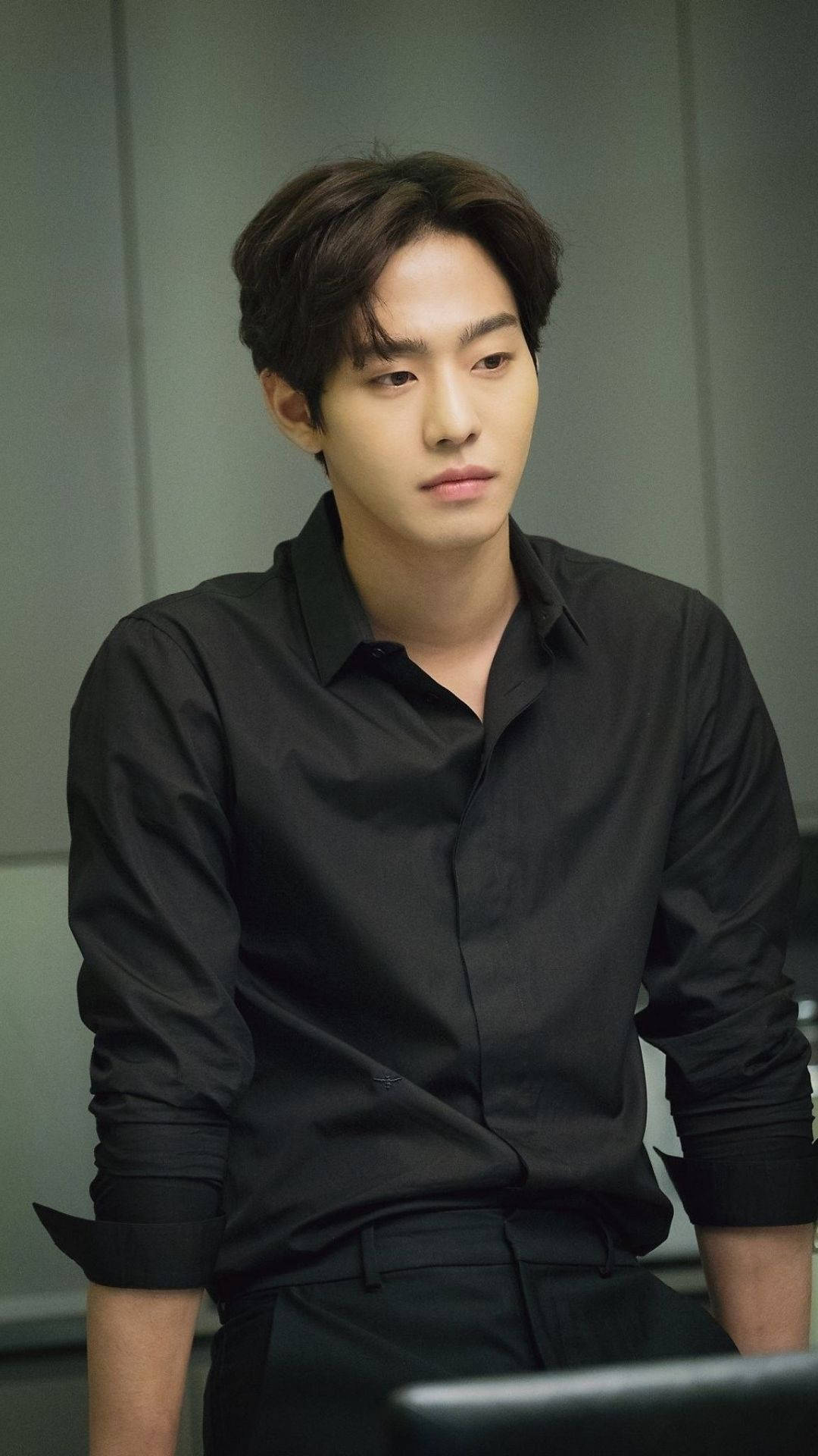 Ahn Hyo Seop 桌布 壁紙 — 一位身穿黑色襯衫的年輕男子在柔和燈光的現代辦公室中沉思地坐著。