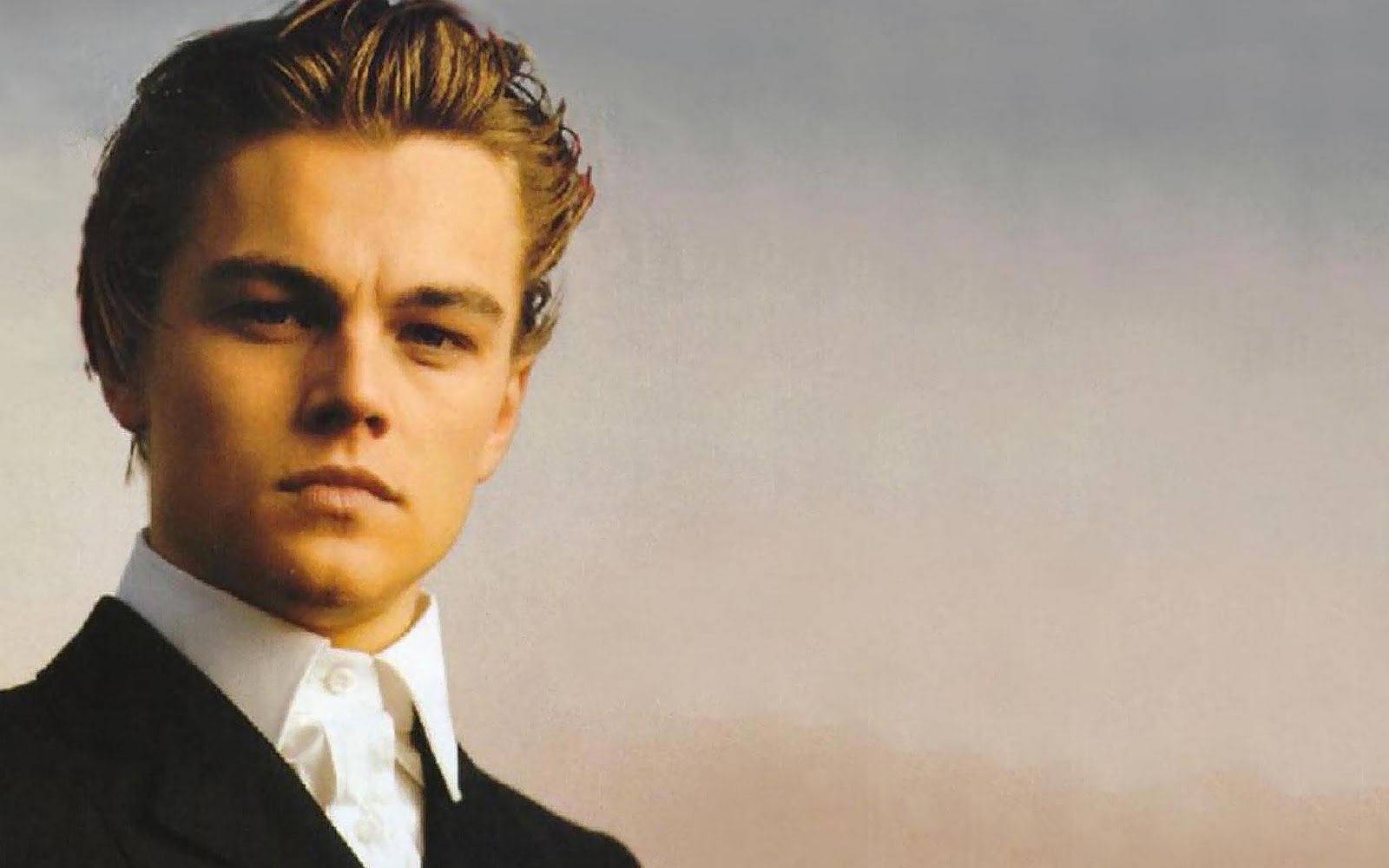 Dicaprio 桌布 壁紙 — 一位身穿黑色西裝和白色襯衫的年輕男子，在柔和的漸變天空下凝視著。