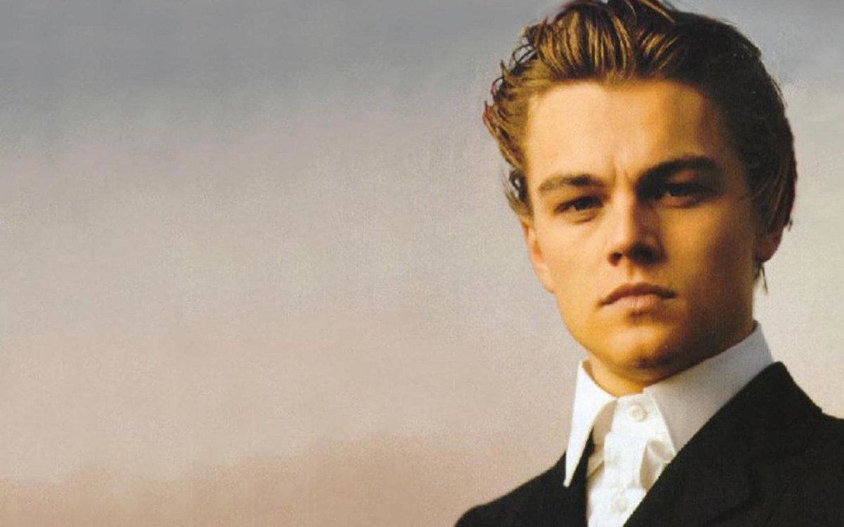 Dicaprio 桌布 壁紙 — 一位身穿黑色西裝和白色襯衫的年輕男子，對著柔和漸變的天空凝視。