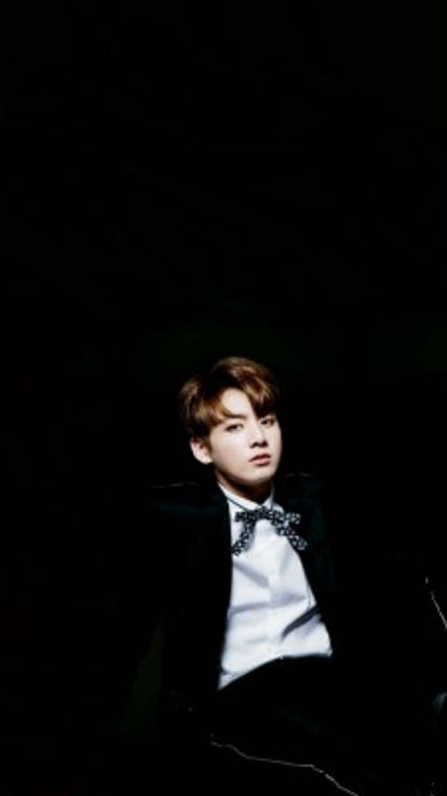 BTS 桌布 壁紙 — 一位身穿黑色西裝和領結的年輕男子在黑暗背景下抬頭仰望，帶有戲劇性的聚光燈效果。