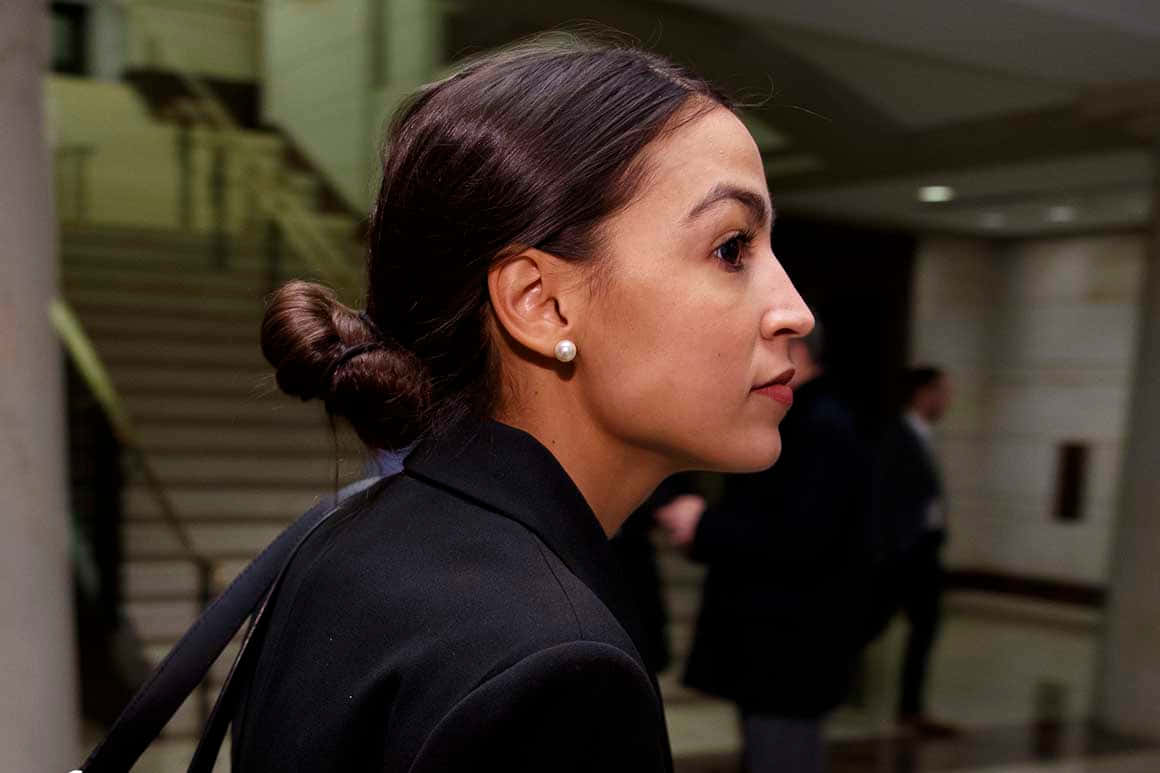 政治 桌布 壁紙 — 一位身穿黑色西裝外套、頭髮盤成髮髻的女性，走過一條現代化的室內走廊，背景有樓梯。