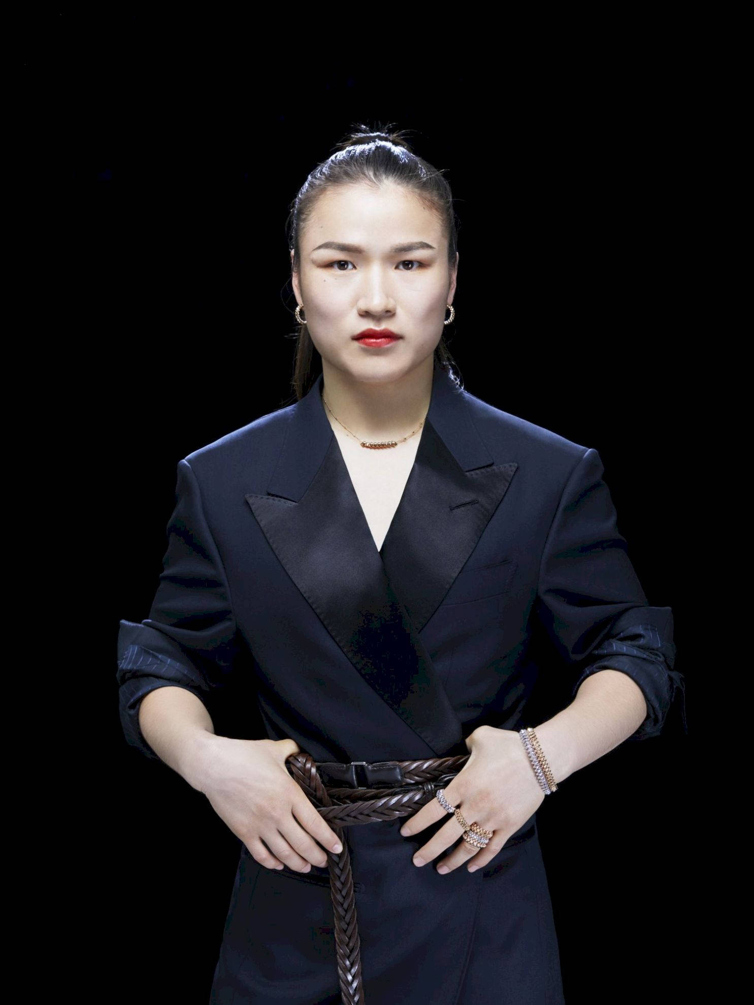 Athletic 桌布 壁紙 — 一位身穿黑色西裝外套搭配辮子腰帶的優雅女性，在純黑背景前自信地站立。