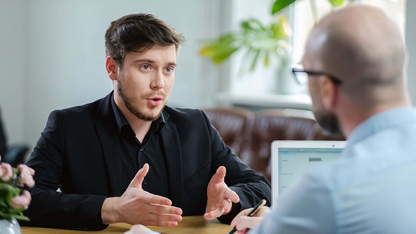 interview 桌布 壁紙 — 一位身穿黑色西裝的年輕男子在木桌上進行商務會議時熱情地做手勢。