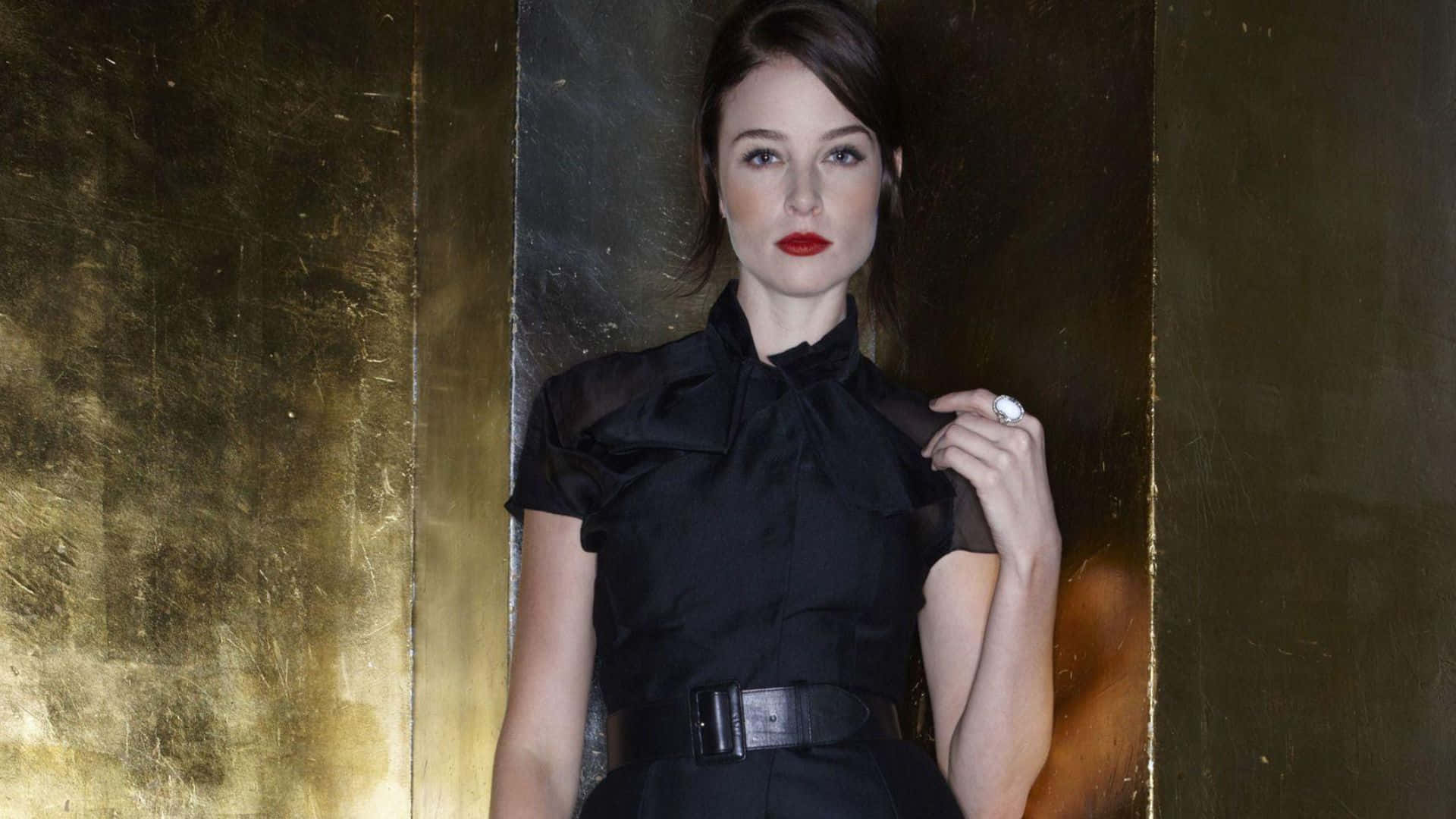 rachel nichols 桌布 壁紙 — 一位身穿黑色連衣裙、紅唇的優雅女士，靠著紋理金牆，手舉到肩上。