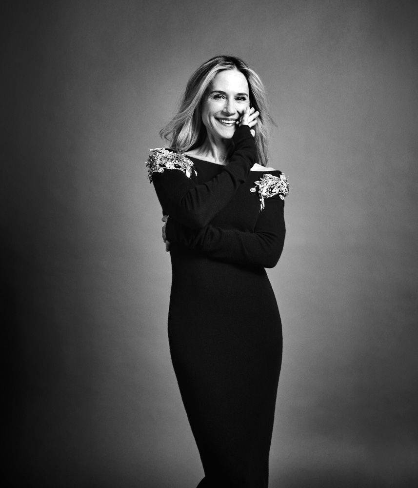 Celebrity 桌布 壁紙 — 一位身穿黑色連衣裙、肩部裝飾華麗的女性在柔和的灰色工作室背景下溫暖地微笑。