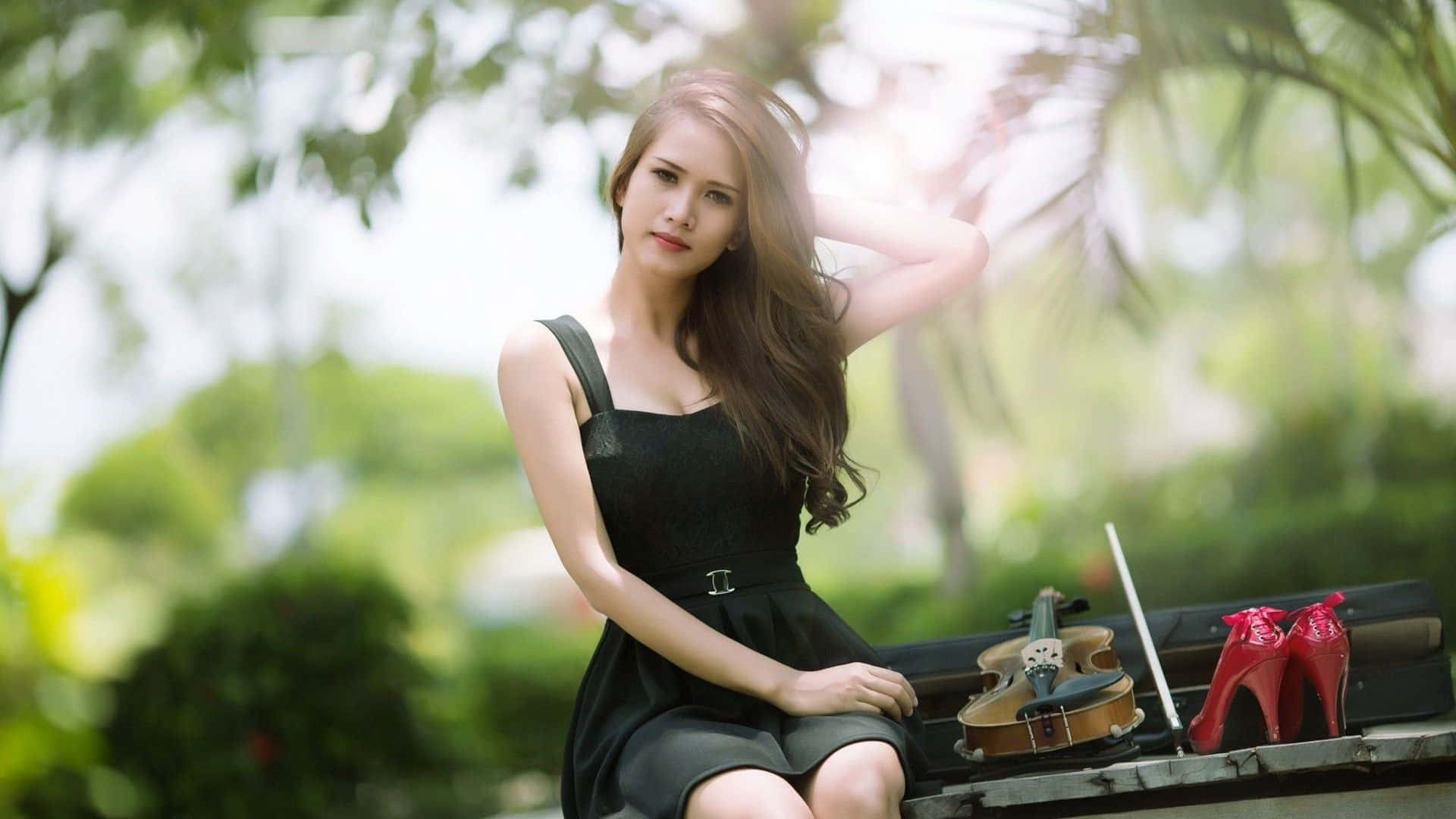桌布 壁紙 — 一位身穿黑色連衣裙的女性坐在戶外的長椅上，旁邊放著小提琴和紅色高跟鞋，沐浴在柔和的陽光中。