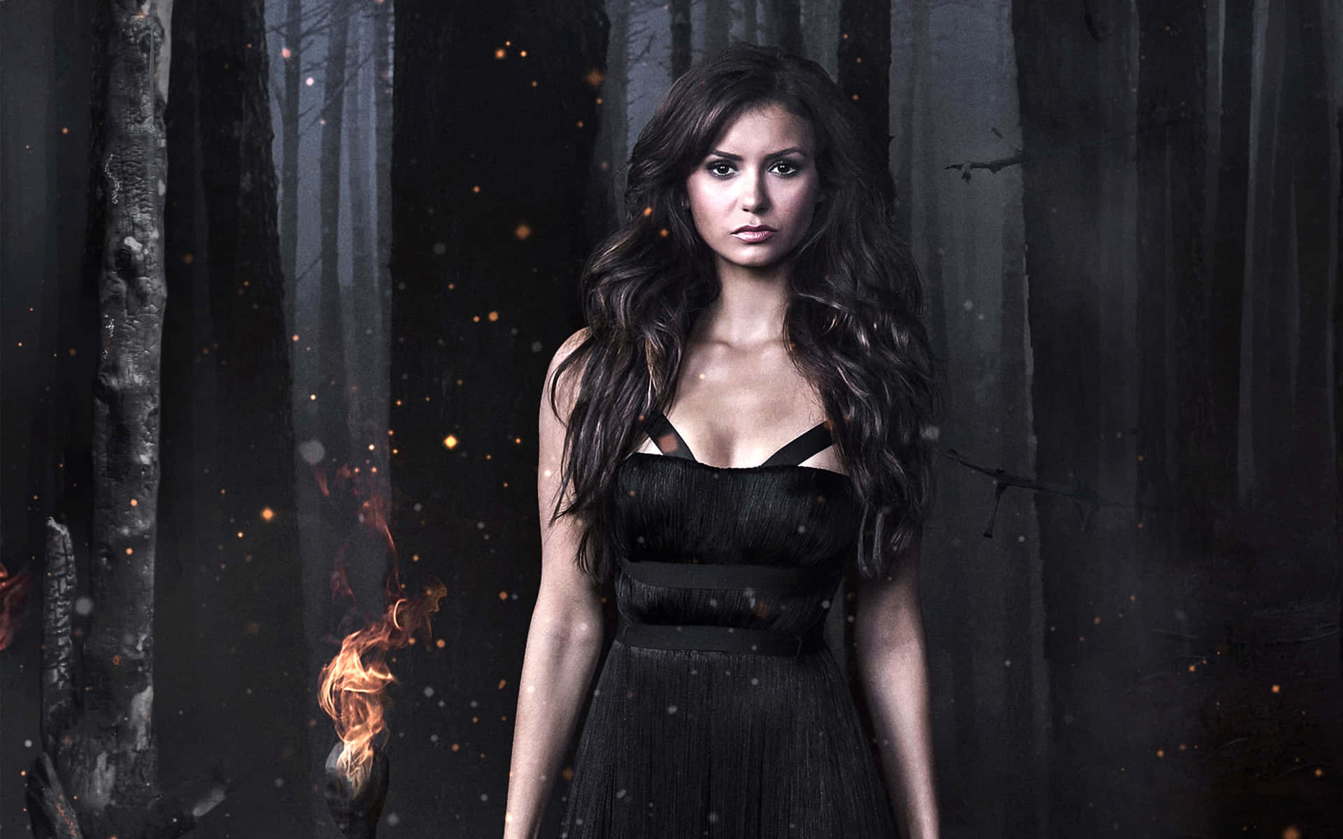 Vampire Diaries Desktop 桌布 壁紙 — 一位身穿黑色連衣裙的女性站在陰暗迷霧的森林中，周圍漂浮著發光的餘燼。