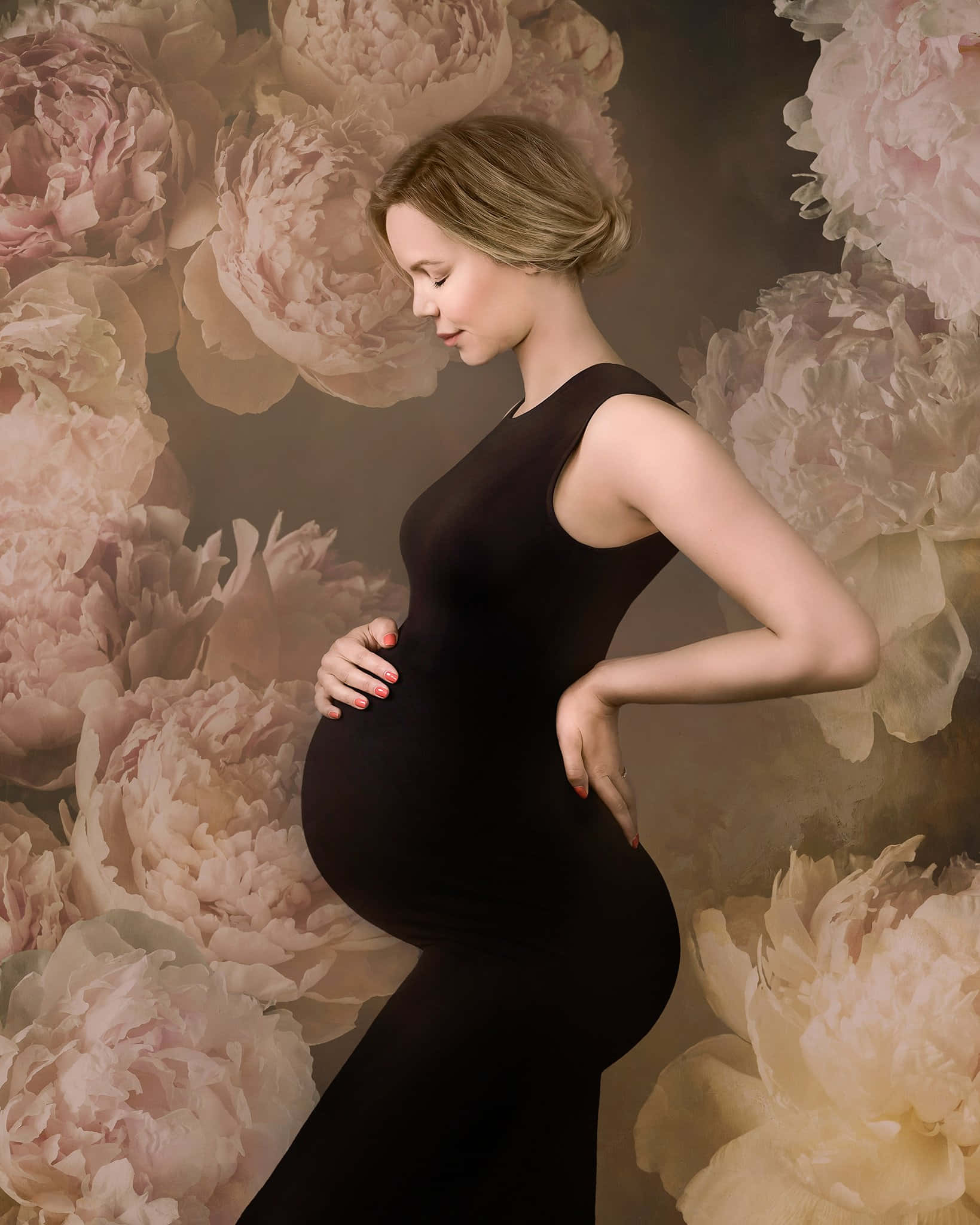 Pregnant 桌布 壁紙 — 一位身穿黑色連衣裙的孕婦，在柔和的粉紅色和奶油色牡丹背景下，輕輕地捧著肚子。