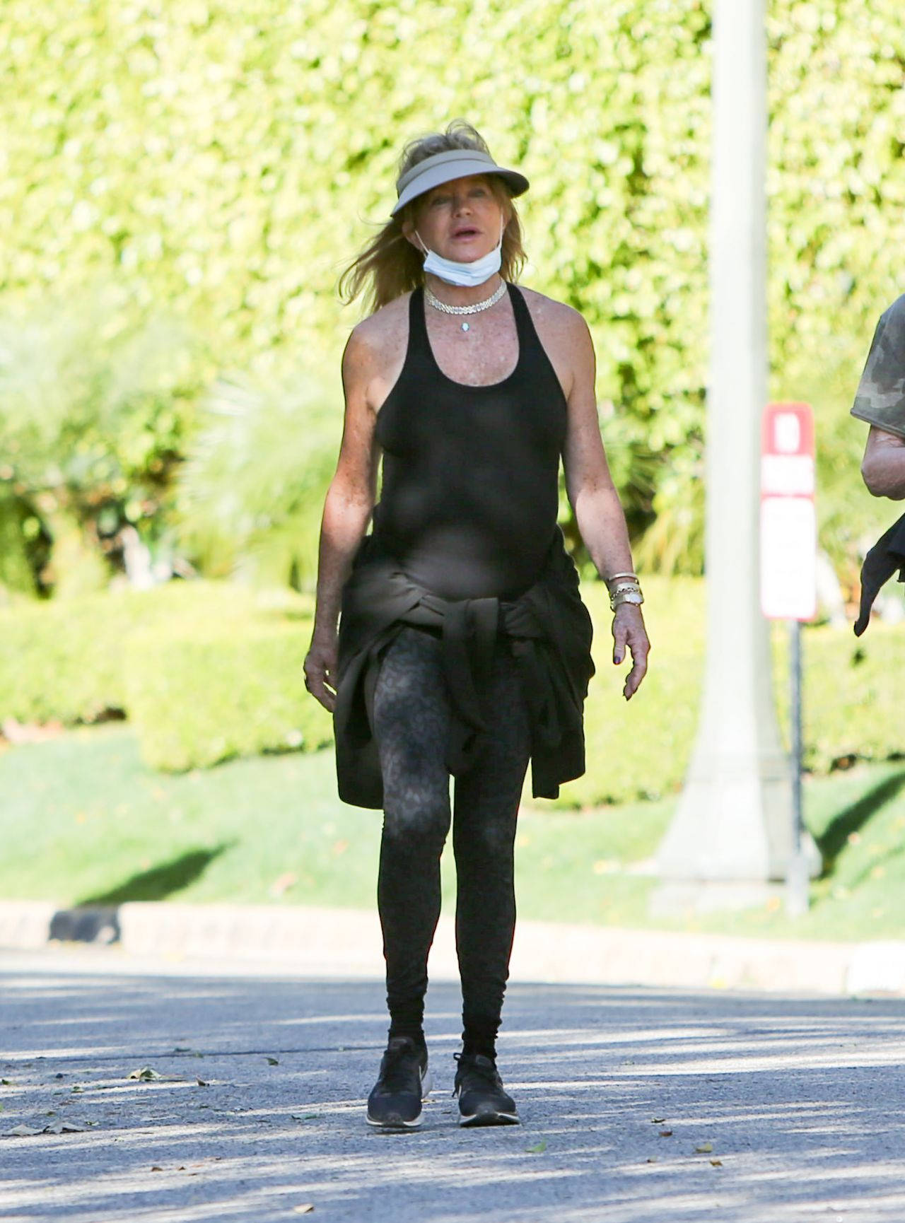 Celebrity 桌布 壁紙 — 一位身穿黑色運動服和遮陽帽的女性在陽光明媚的日子裡在戶外散步，身後有綠色樹葉。