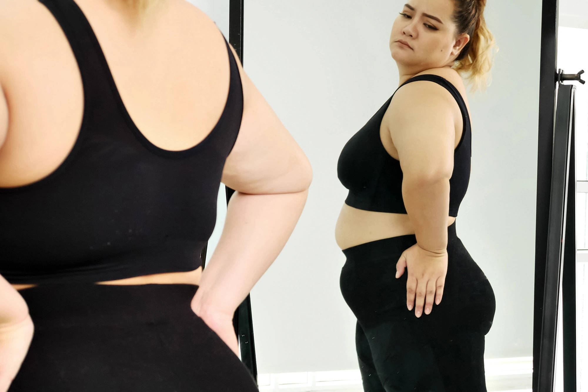 Fat Woman 桌布 壁紙 — 一位身穿黑色運動服的女士，帶著沉思的表情凝視著鏡中的倒影。