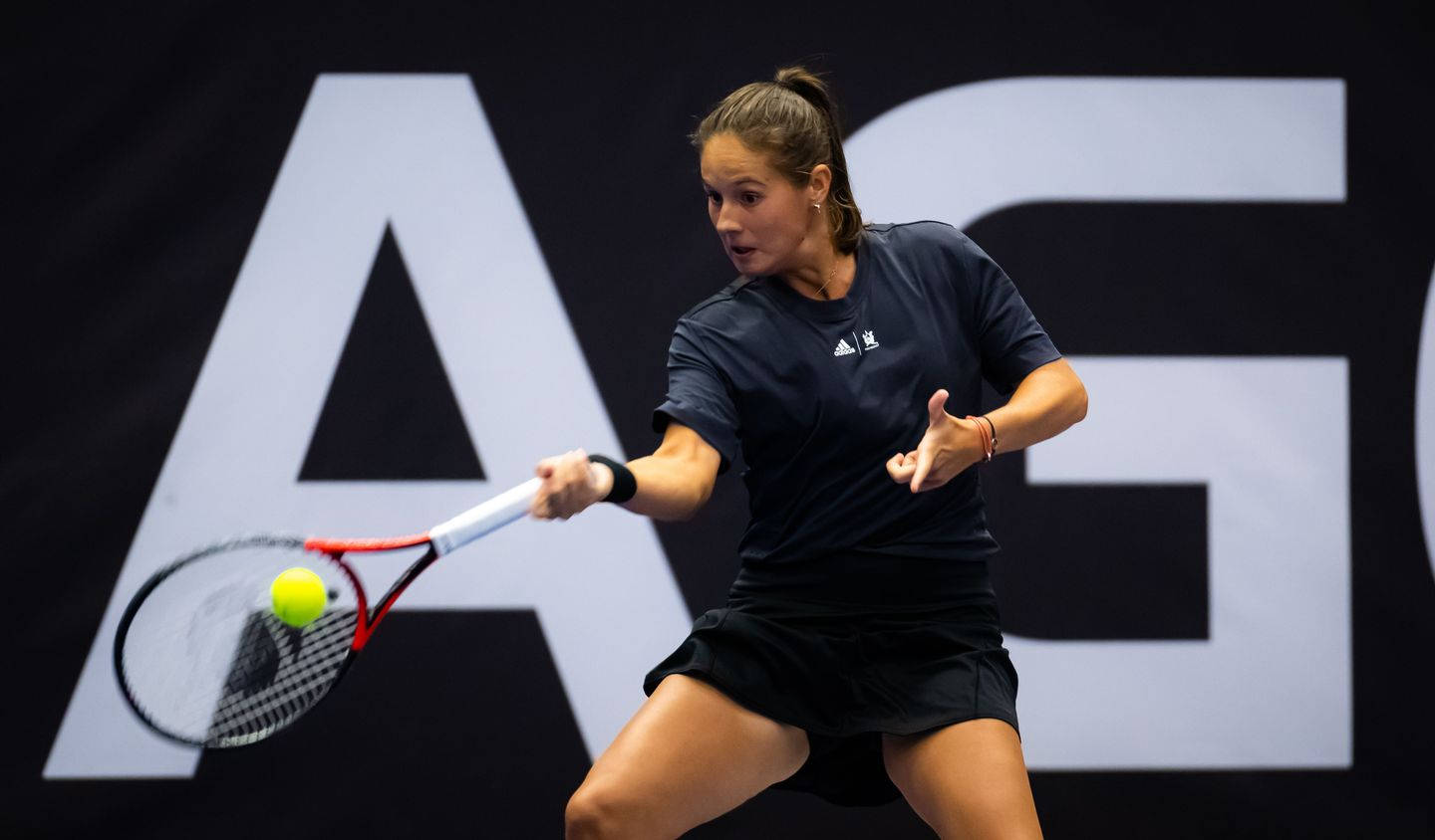 Athletic 桌布 壁紙 — 一位身穿黑色運動服的女網球選手揮動球拍，擊打一個亮黃色的球，背景是純黑色並帶有大型白色字母。