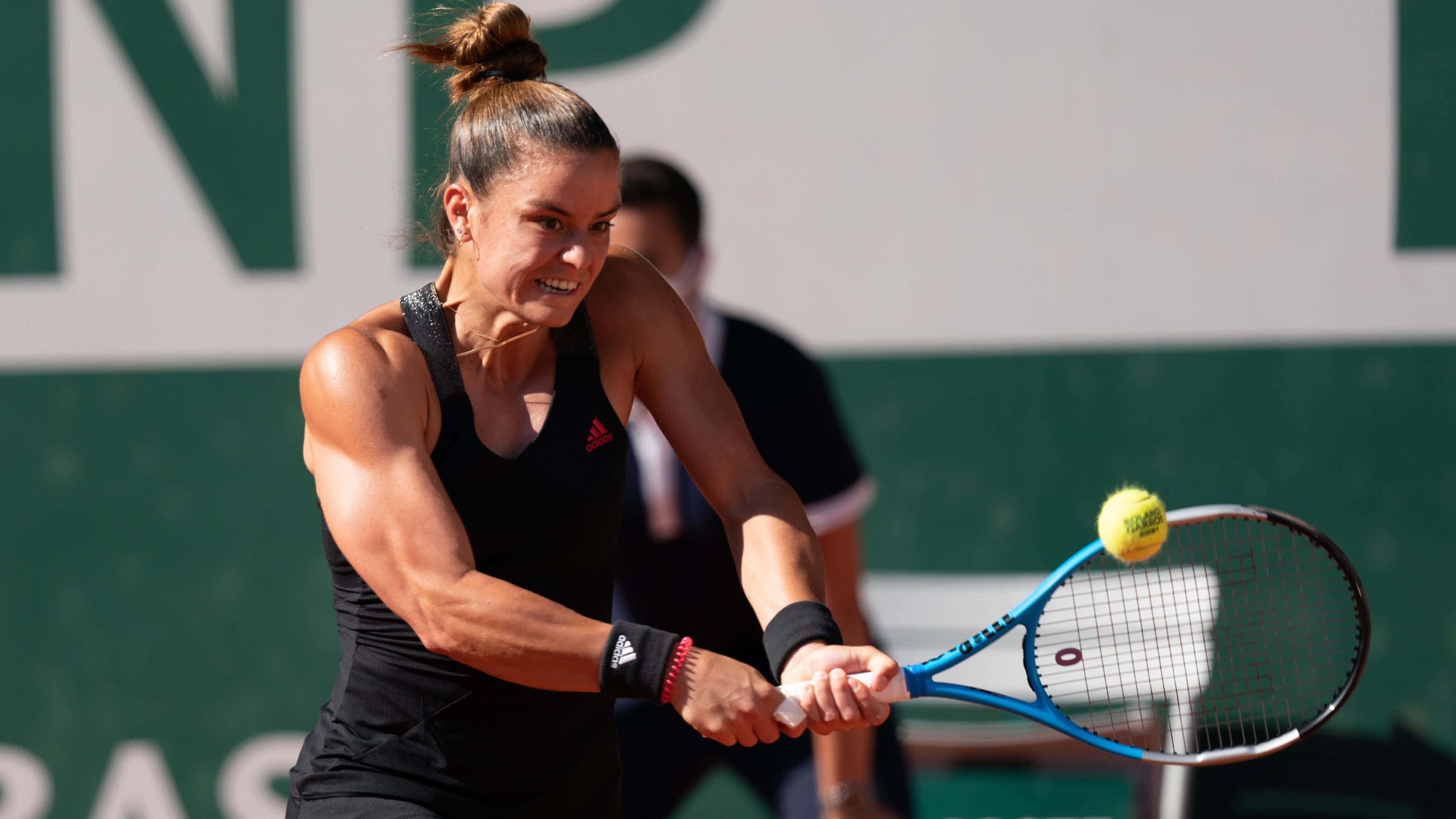 Athletic 桌布 壁紙 — 一位身穿黑色運動裝備的女網球運動員在明亮的日光下，在紅土球場上揮動藍色球拍擊打黃色球。