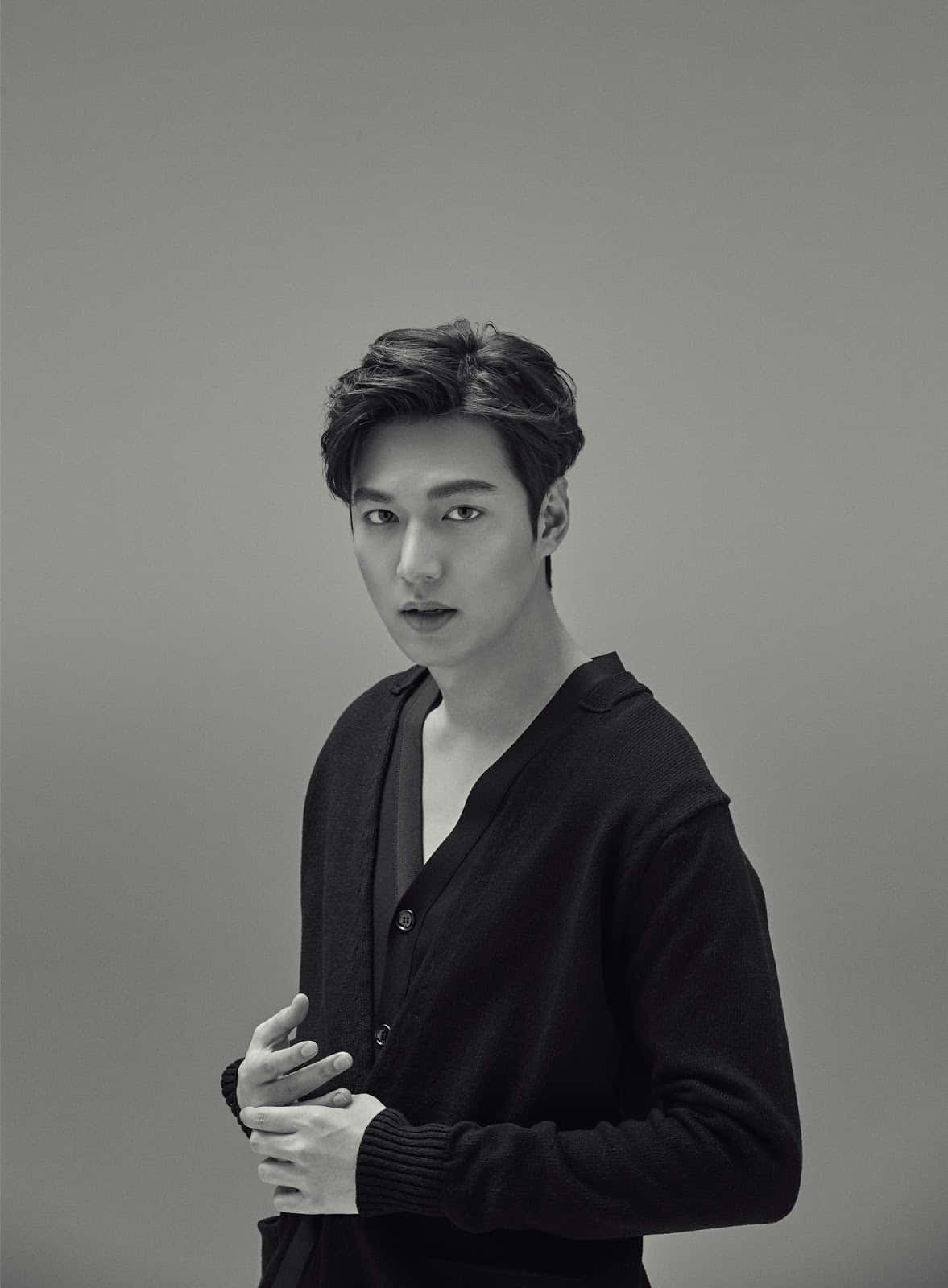 Lee Min Ho 桌布 壁紙 — 一位身穿黑色開襟衫的年輕男子站在純灰色背景前，直視前方，雙手交握在腰部附近。