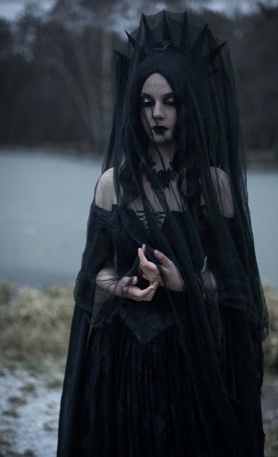 Witch Costumes 桌布 壁紙 — 一位身穿黑色面紗和蕾絲長袍的哥德式女性，站在霧氣瀰漫的湖邊，背景是光禿的樹木。