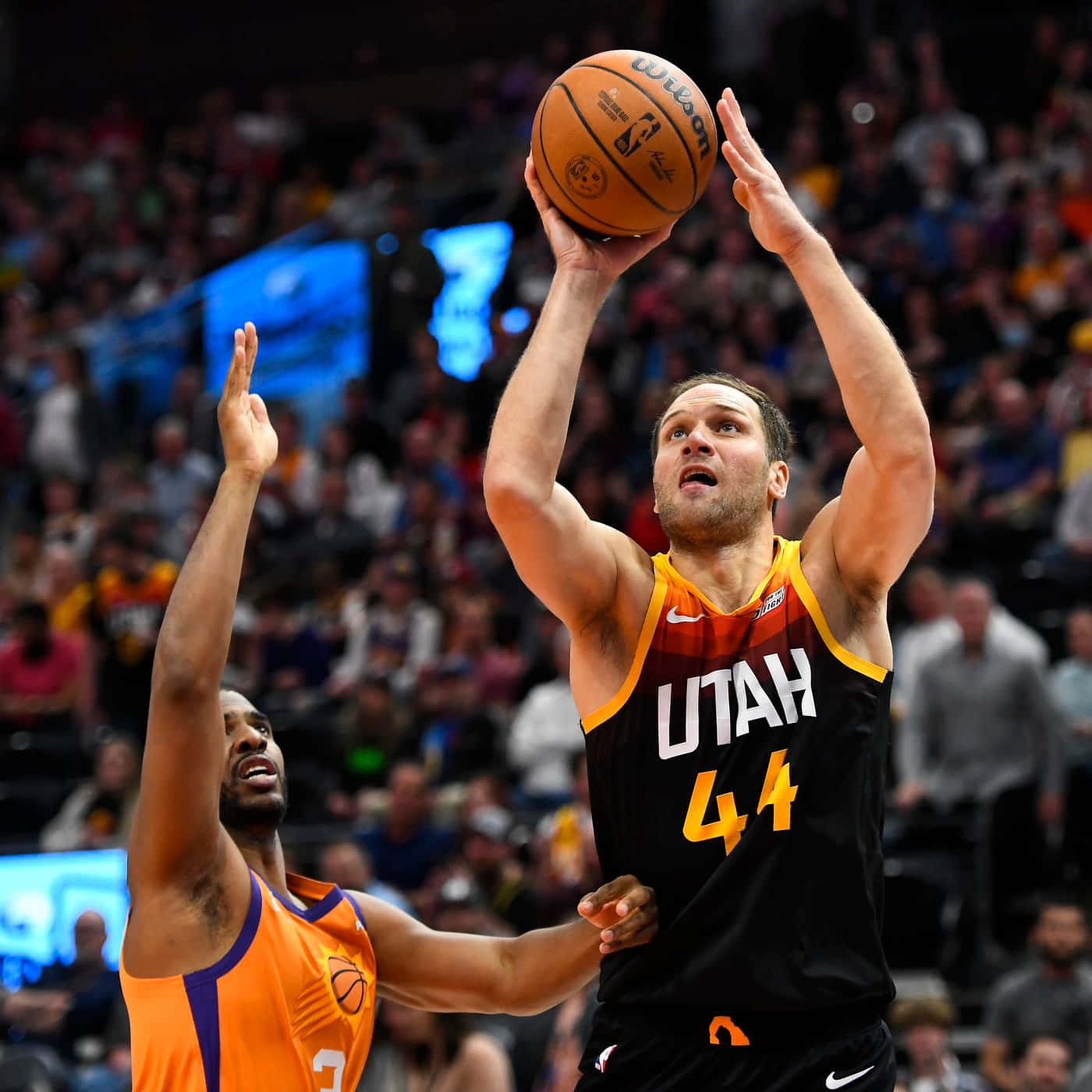 NBA 桌布 壁紙 — 一位身穿黑黃球衣的猶他爵士球員正在投籃，而一位身穿橙色球衣的鳳凰城太陽防守球員在場館燈光下干擾投籃。
