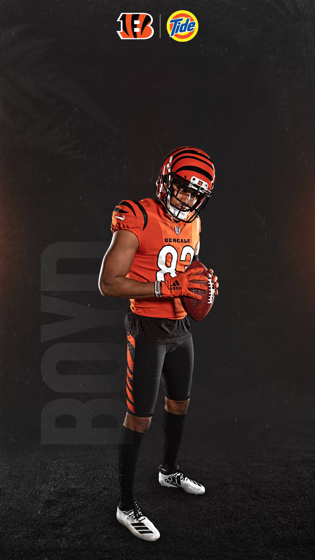Bengals 桌布 壁紙 — 一位辛辛那提猛虎隊美式足球員身穿橙黑制服，在帶有品牌標誌的深色紋理背景前抱著一個足球。