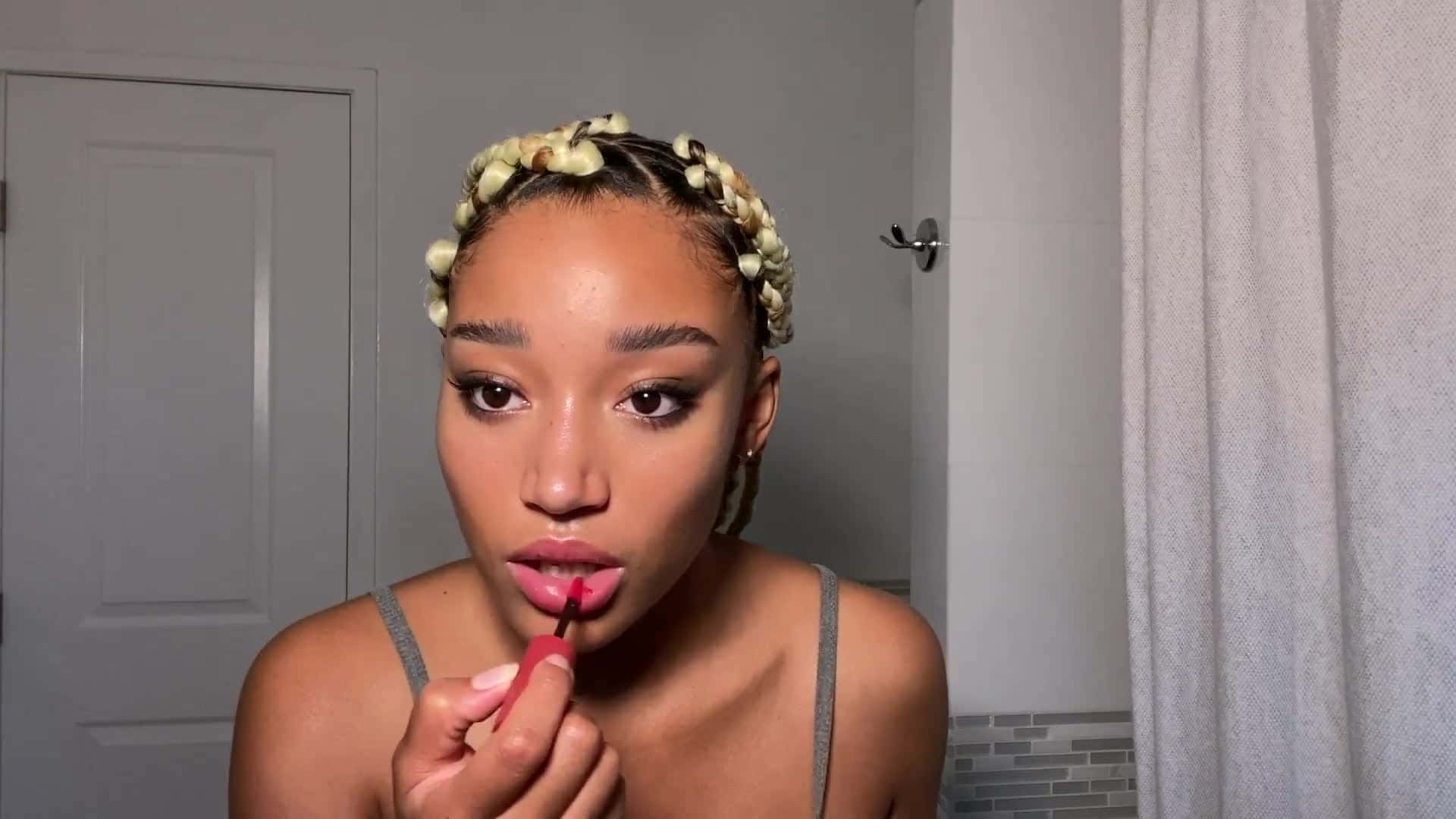 Makeup 桌布 壁紙 — 一位辮子上飾有花朵的女性正在浴室鏡子前塗抹大膽的紅色唇膏。