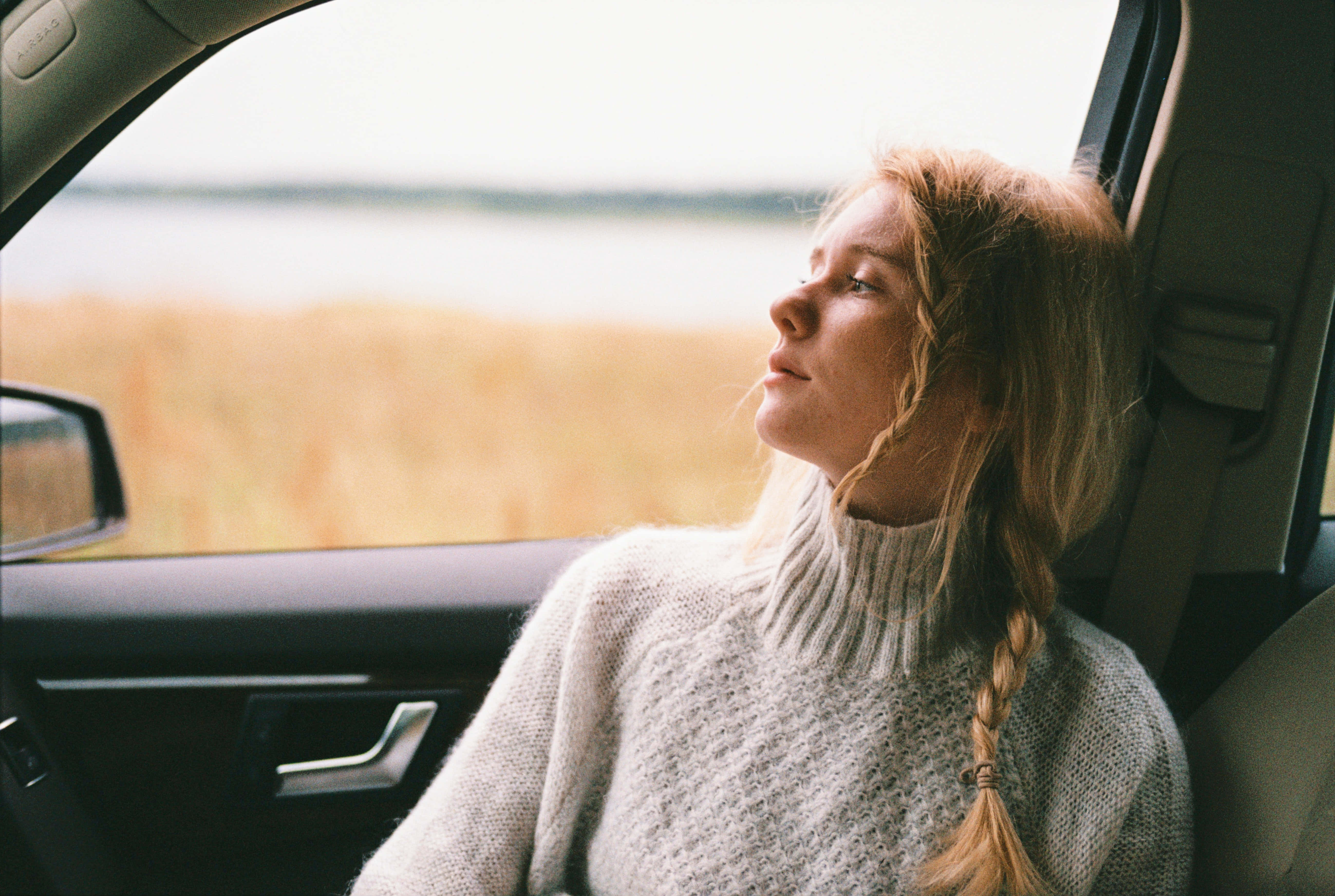 road trip 桌布 壁紙 — 一位辮子年輕女子將頭靠在車窗上，平靜地望著外面金色的田野。