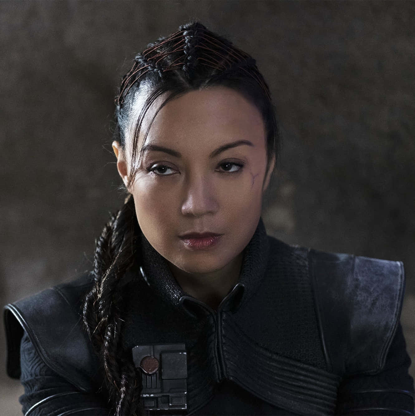 Ming Na Wen 桌布 壁紙 — 一位辮子頭髮、帶有疤痕的兇猛女戰士，身穿暗色盔甲，在粗糙的石牆前凝視著。