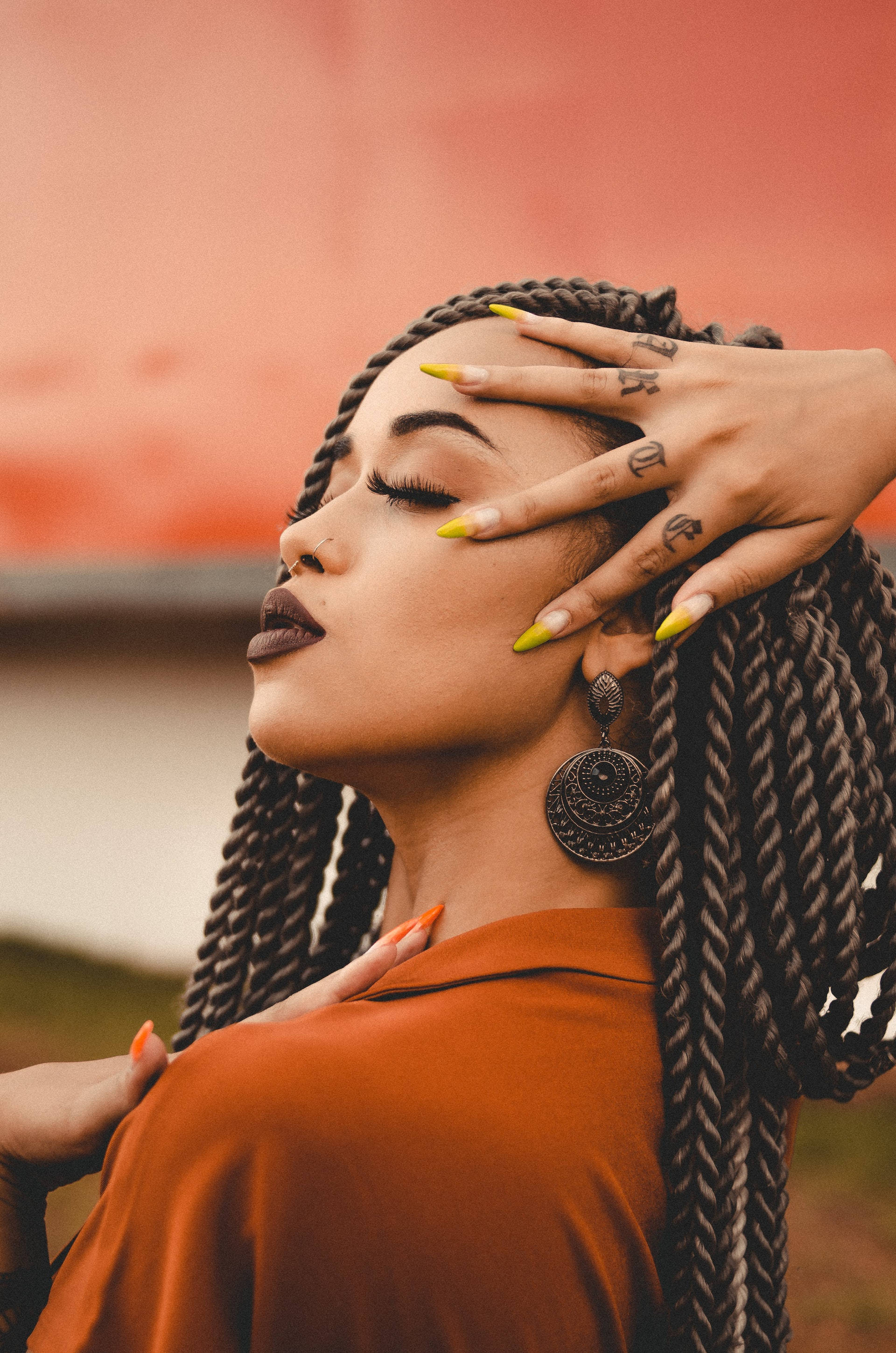 Black Girl 桌布 壁紙 — 一位辮子頭髮、黃色指甲的女性，在溫暖的橙色背景下輕輕觸碰臉頰。