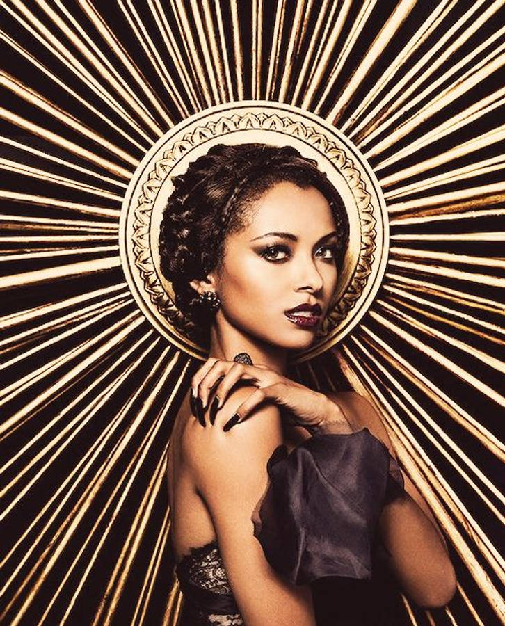 Vampire Diaries 桌布 壁紙 — 一位辮子頭髮和深色唇膏的女性自信地凝視著帶有黑色和金色條紋的燦爛金色光環。