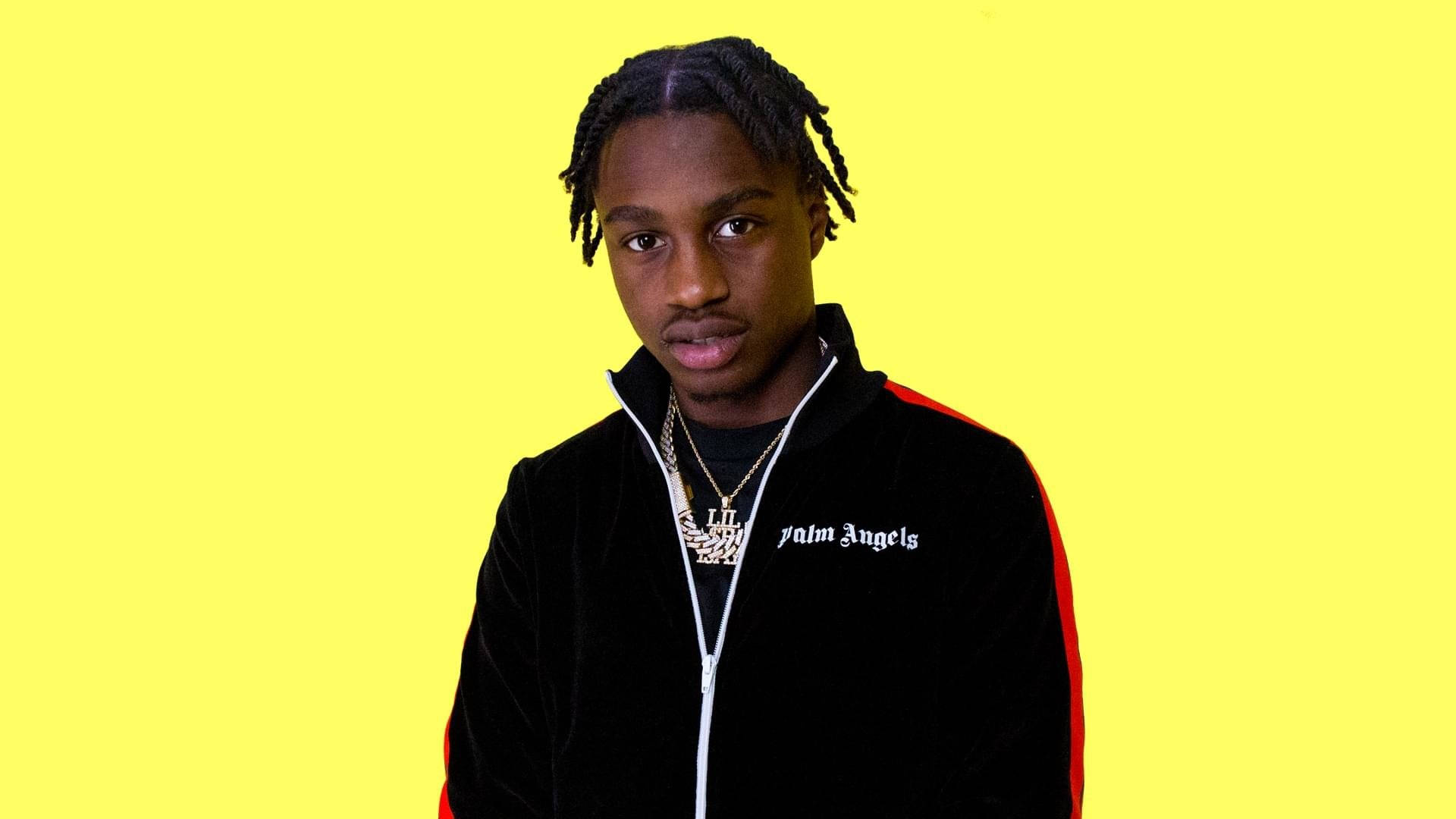 Lil Tjay 桌布 壁紙 — 一位辮子頭髮的年輕男子穿著黑色天鵝絨Palm Angels外套，背景為明亮的黃色。