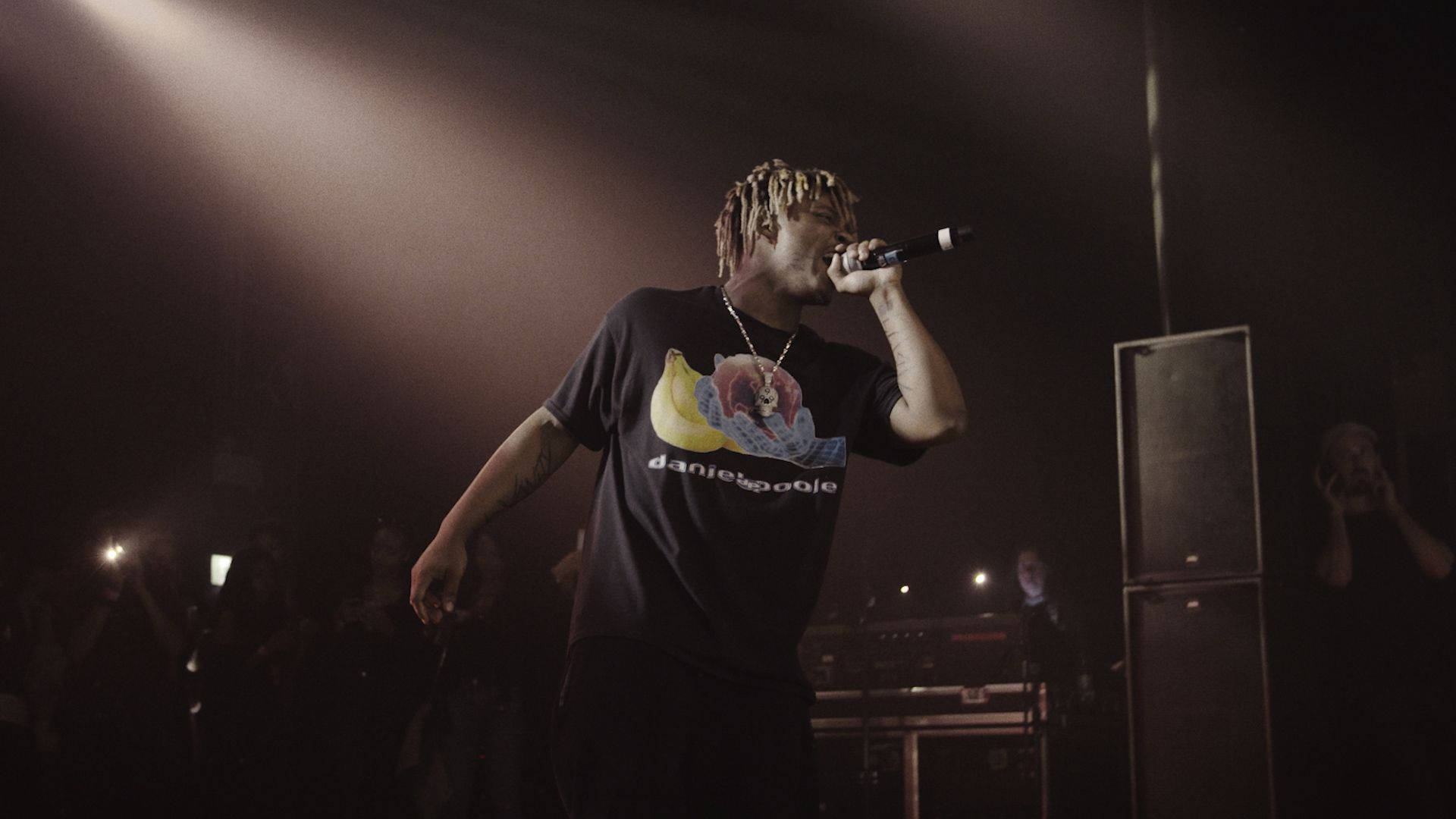 說唱歌手在聚光燈下舞台上表演，背景有觀眾。 — Juice Wrld 壁紙