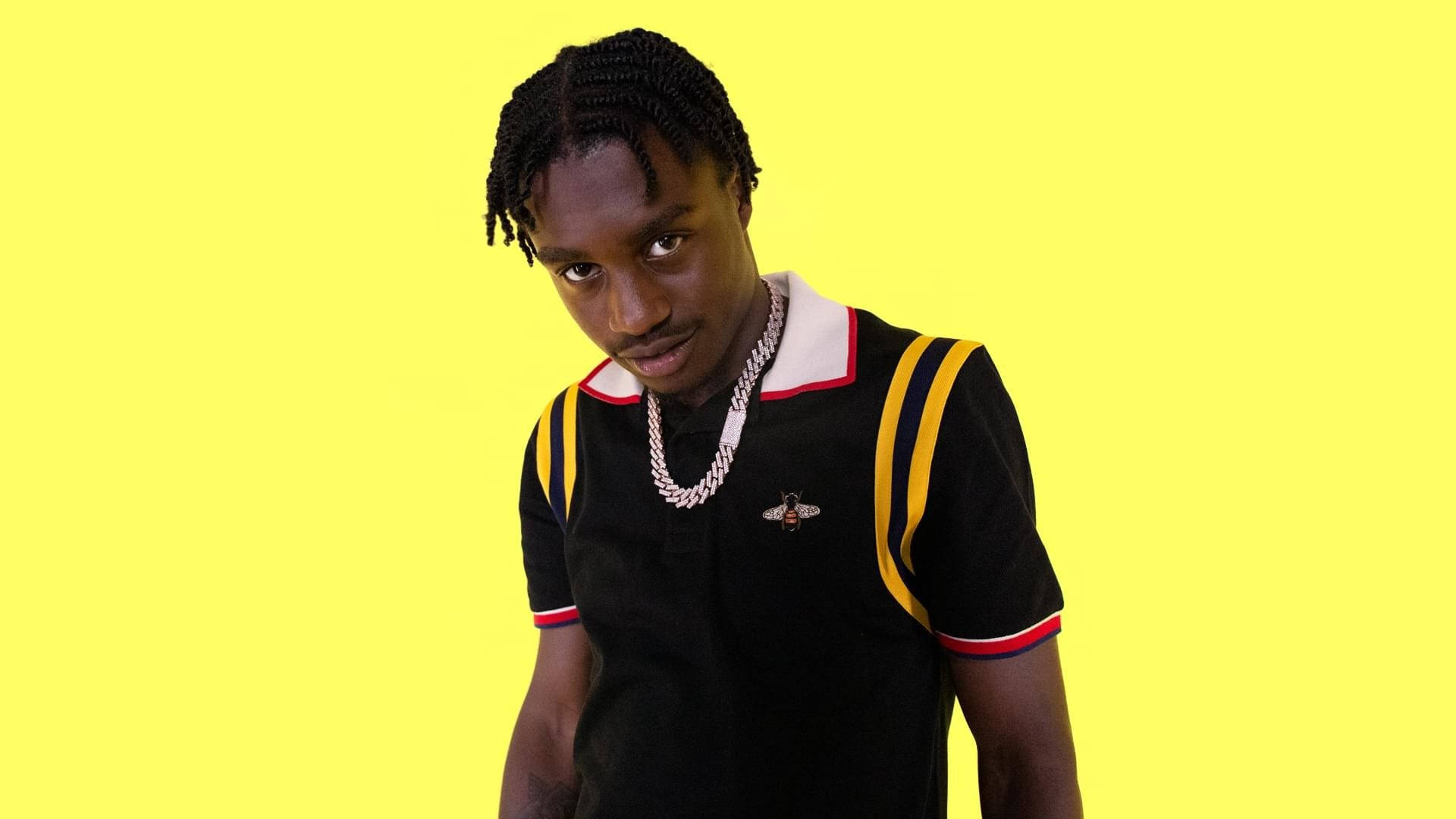 Lil Tjay 桌布 壁紙 — 一位辮髮年輕男子穿著帶有黃色條紋的黑色Polo衫和銀色項鍊，背景為亮黃色。