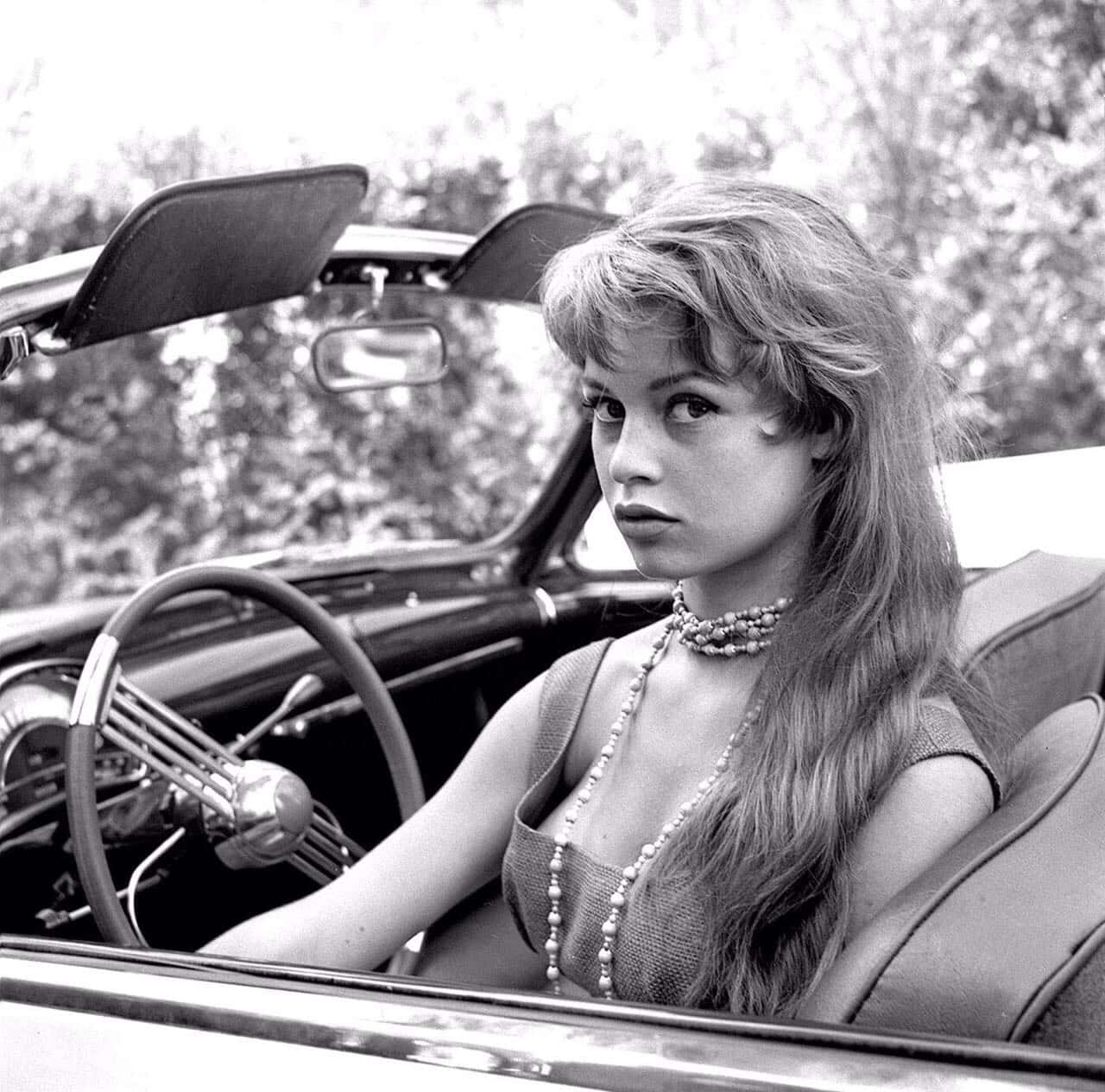 1950s 桌布 壁紙 — 一位迷人女性坐在復古敞篷車中，以大膽的表情專注地凝視著相機。