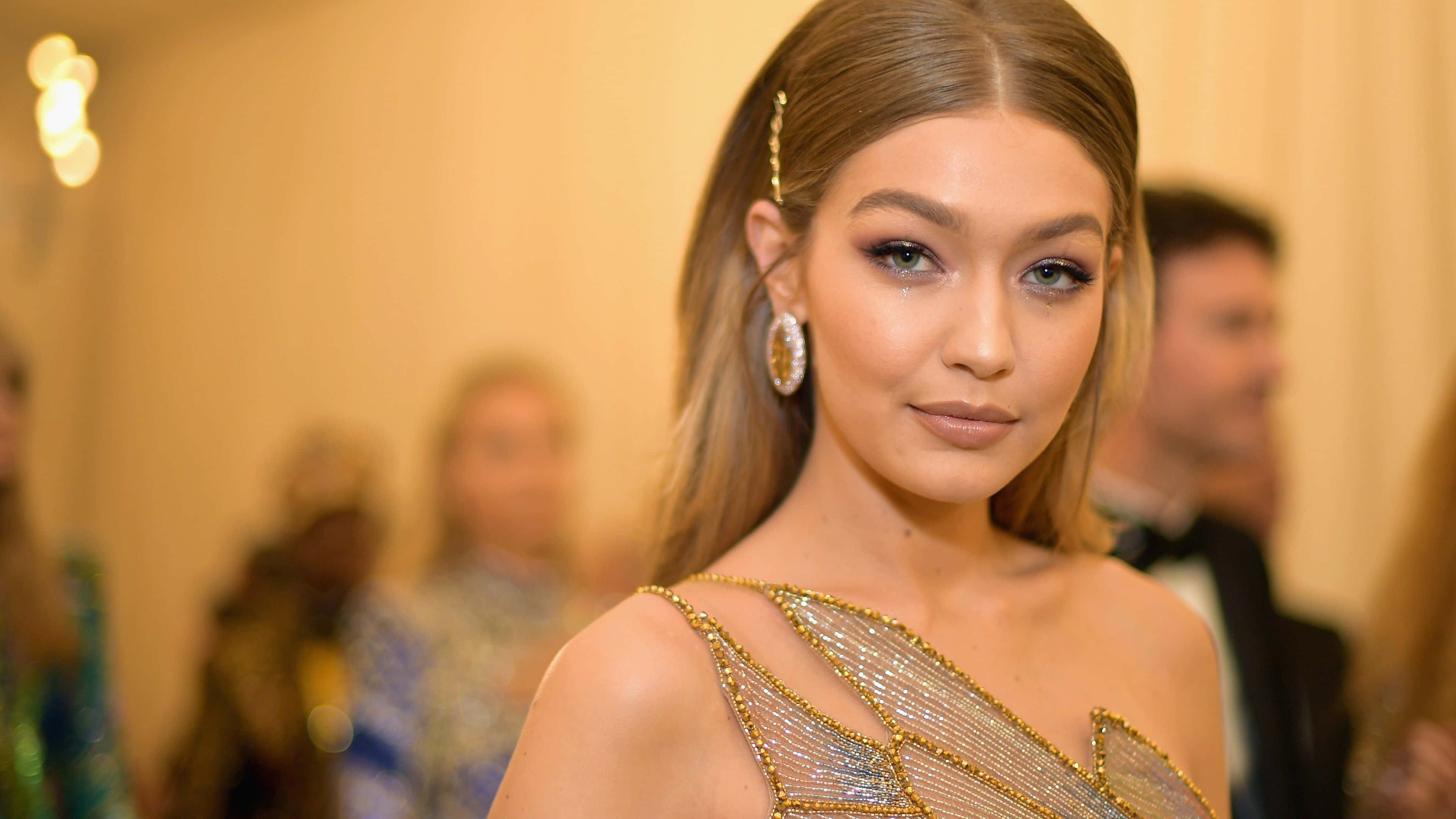 Met Gala 桌布 壁紙 — 一位迷人的女士穿著閃閃發光的金色珠飾長裙，在正式活動中自信地擺姿勢。