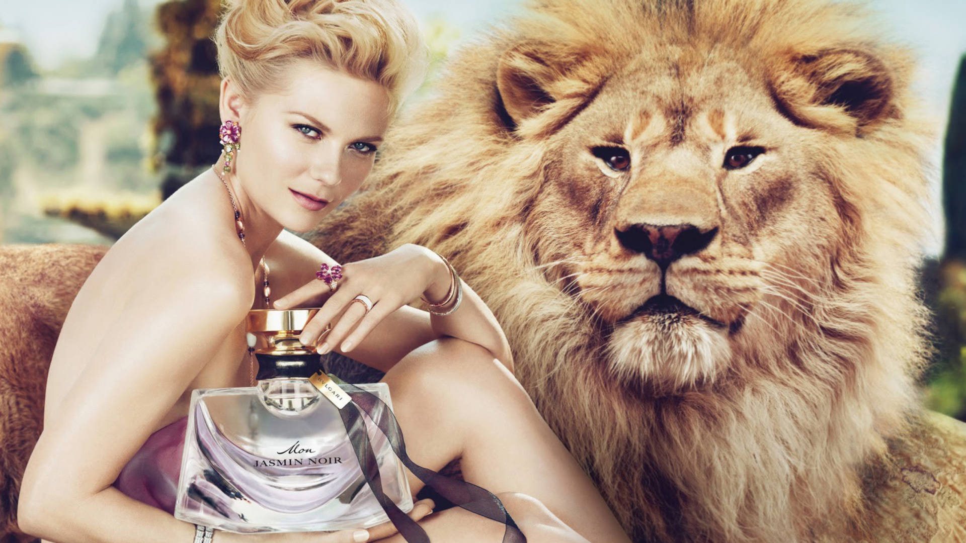 Bvlgari 桌布 壁紙 — 一位迷人的金髮女士佩戴優雅珠寶，在茂密的戶外環境中，手持香水瓶，旁邊是一頭雄偉的雄獅。
