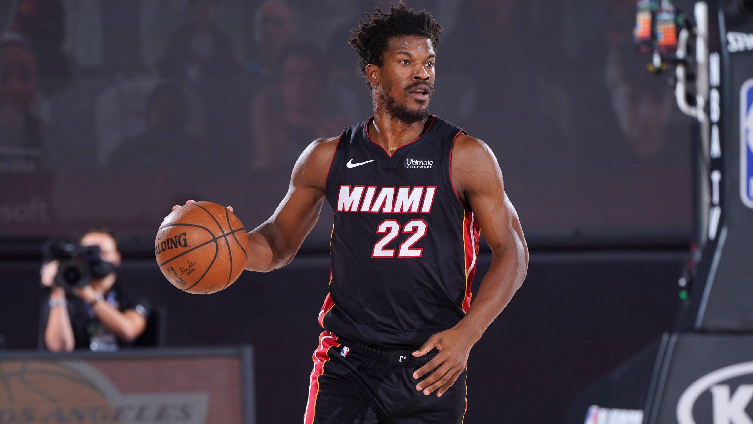 jimmy 桌布 壁紙 — 一位邁阿密熱火籃球運動員身穿黑色球衣，號碼22，在明亮的場館燈光下於激烈比賽中運球。