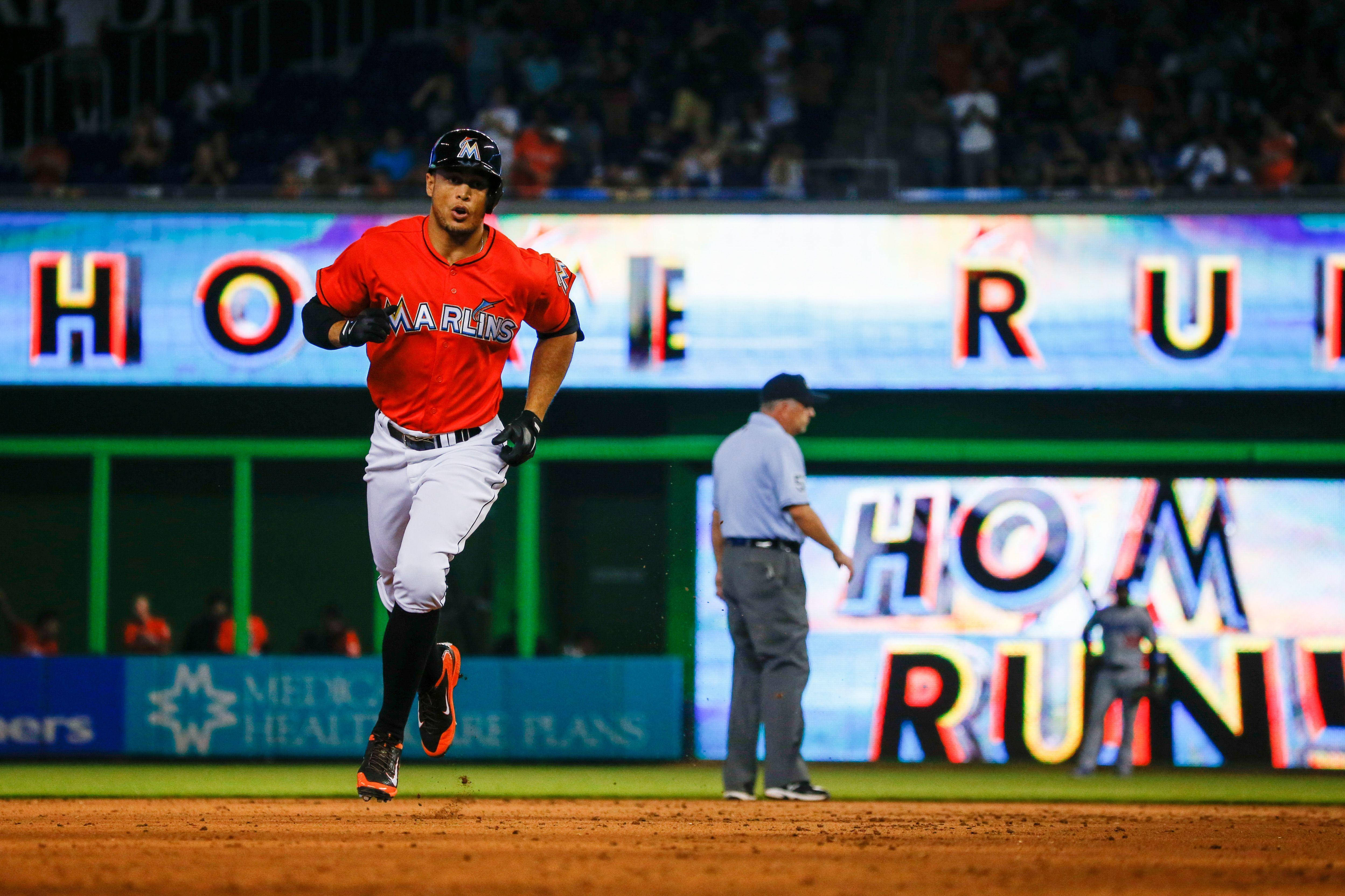 photography 桌布 壁紙 — 一位邁阿密馬林魚棒球選手在球場燈光下，身後『全壘打』標誌閃耀，勝利的衝過內野泥地。