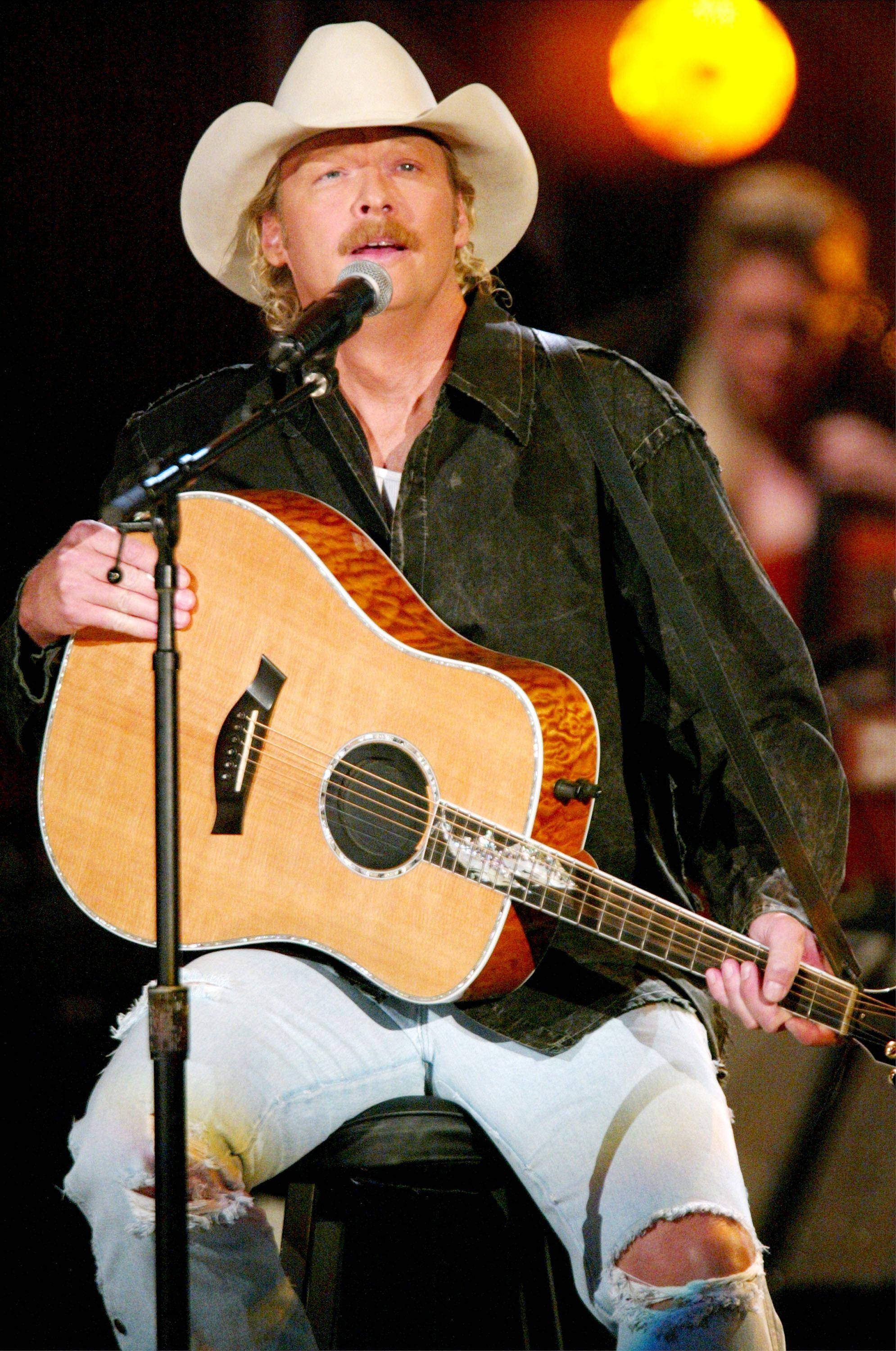 Alan Jackson 桌布 壁紙 — 一位鄉村歌手戴著白色牛仔帽和破洞牛仔褲，在溫暖的舞台燈光下彈奏原聲吉他。